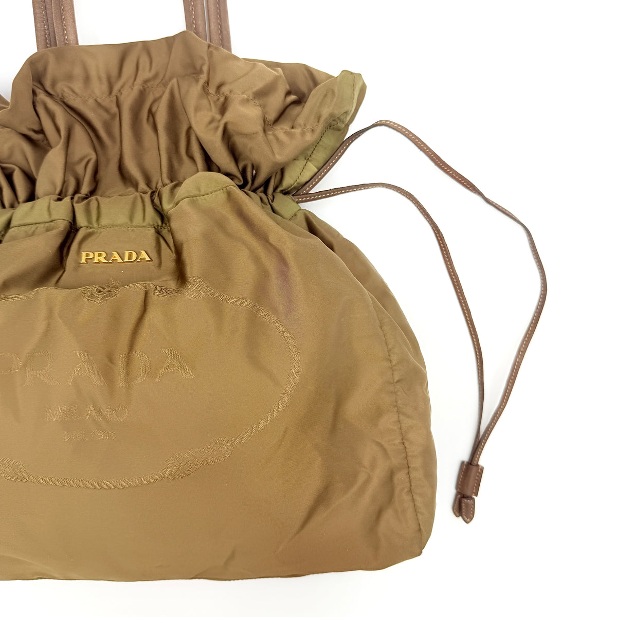 Prada Tessuto brown nylon drawstring shoulder bag with leather handles and gold logo detail, photographed against a white background.