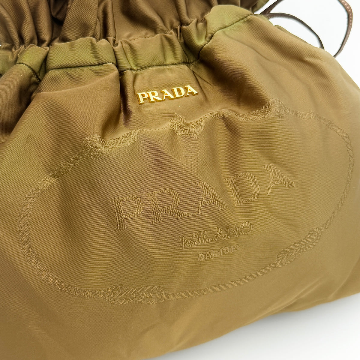 Prada Tessuto brown nylon drawstring shoulder bag with leather handles and gold logo detail, photographed against a white background.