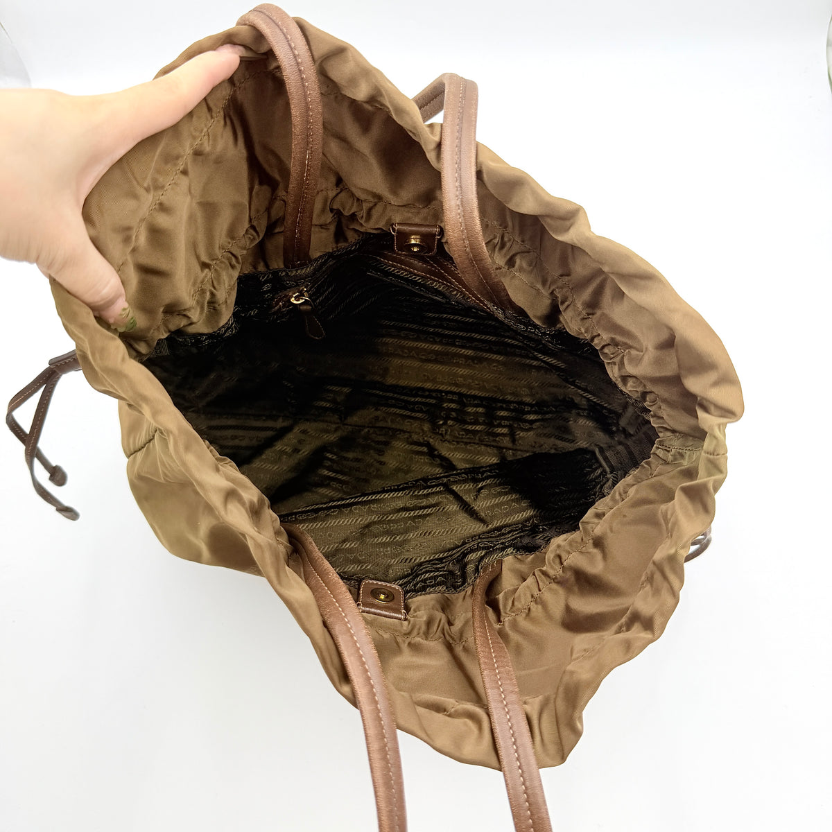 Prada Tessuto brown nylon drawstring shoulder bag with leather handles and gold logo detail, photographed against a white background.