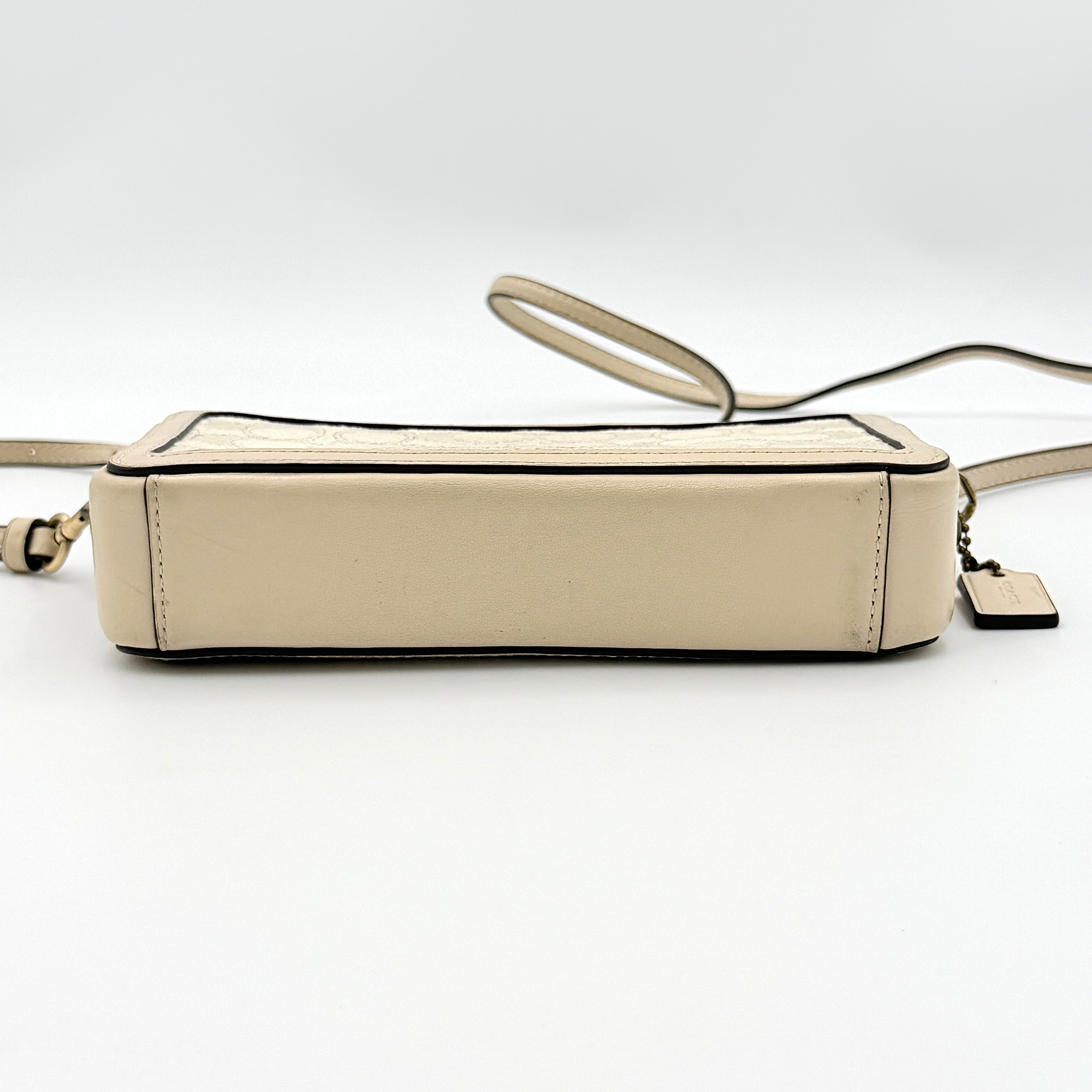 Coach Signature Kira Crossbody Bag in beige and white jacquard with leather trim and adjustable strap displayed against a white background.