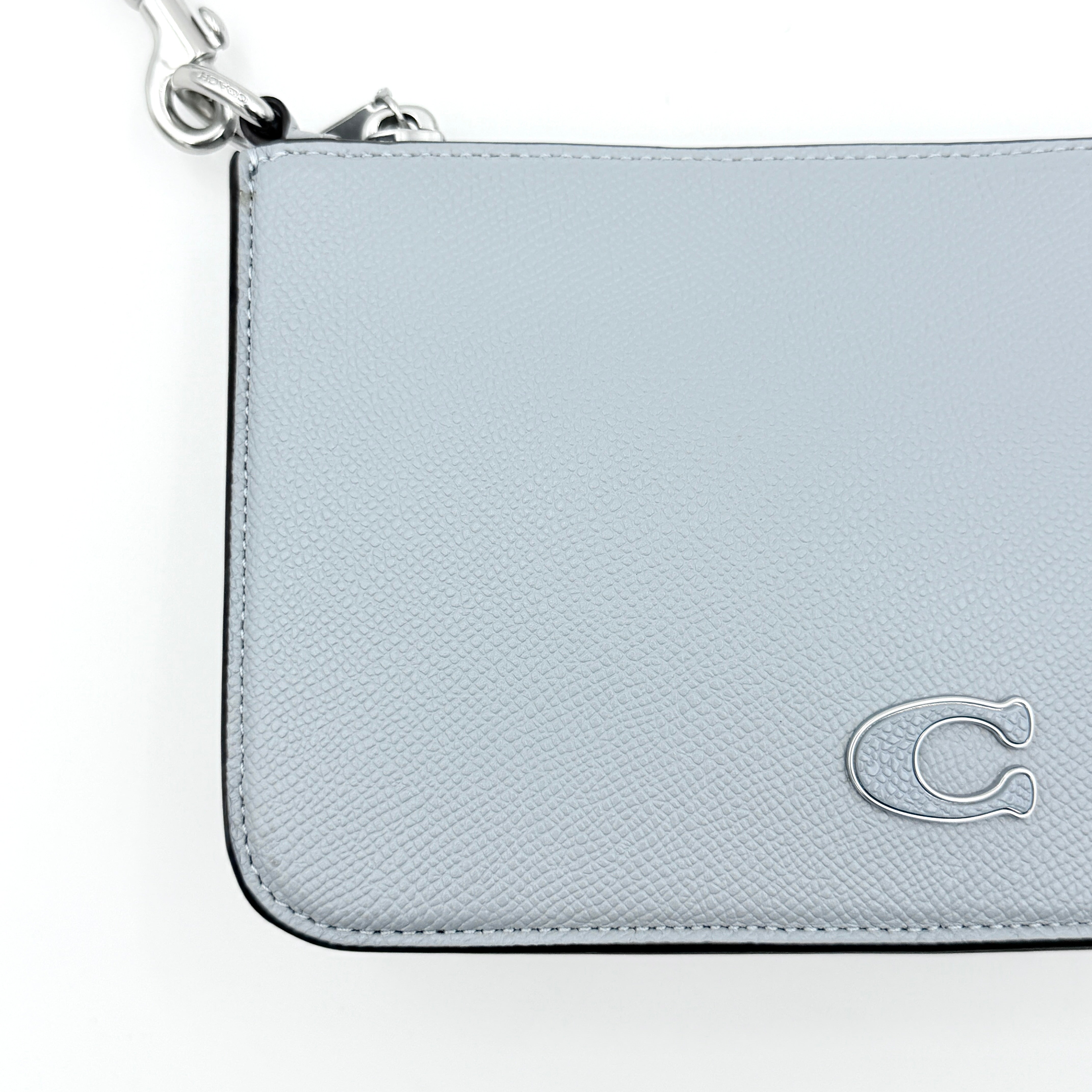 Sky blue Coach grained leather shoulder bag with silver-tone C plaque and short strap, displayed against a white background.