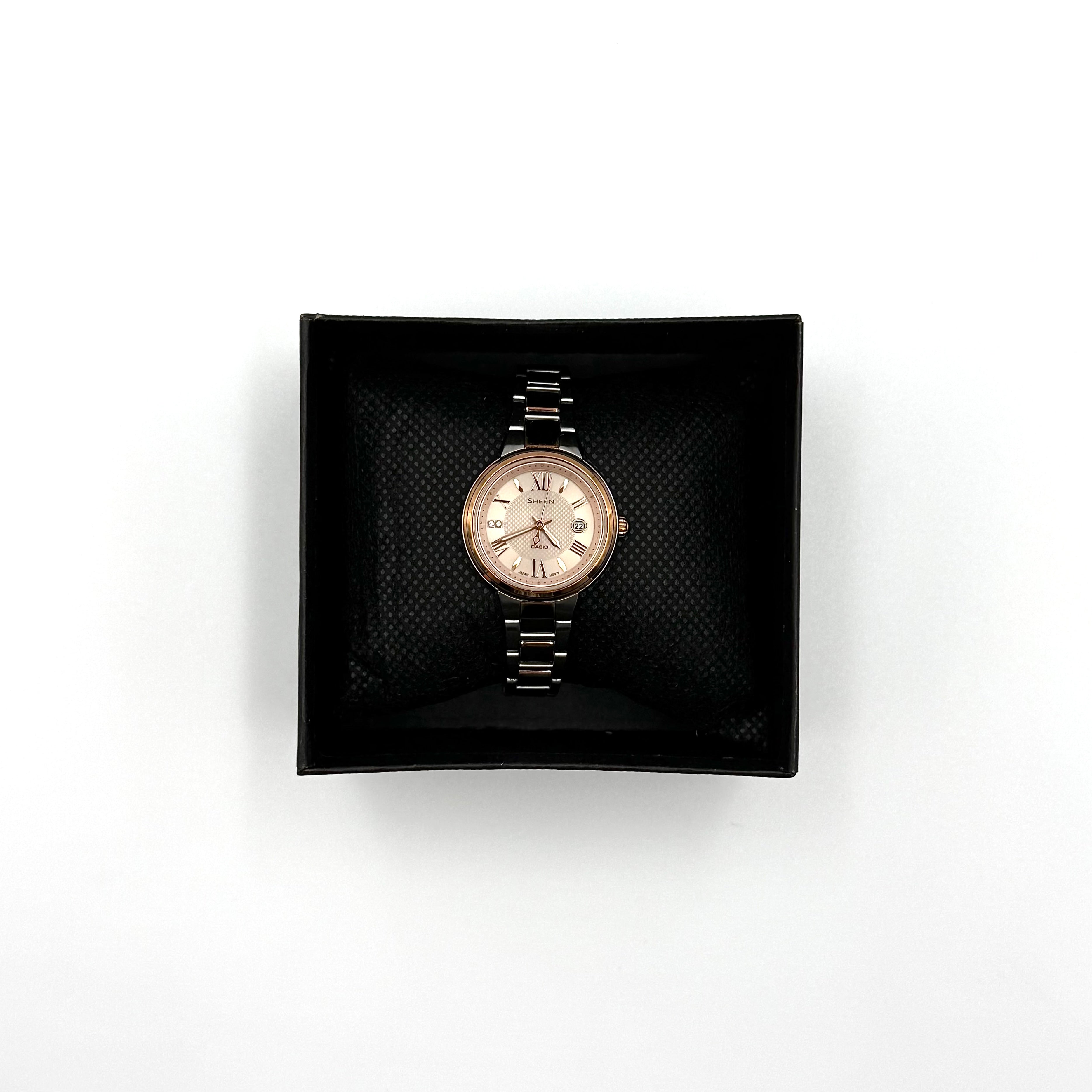Casio Sheen SHE-4516 stainless steel watch with a rose gold and silver bracelet displayed on a black cushion.