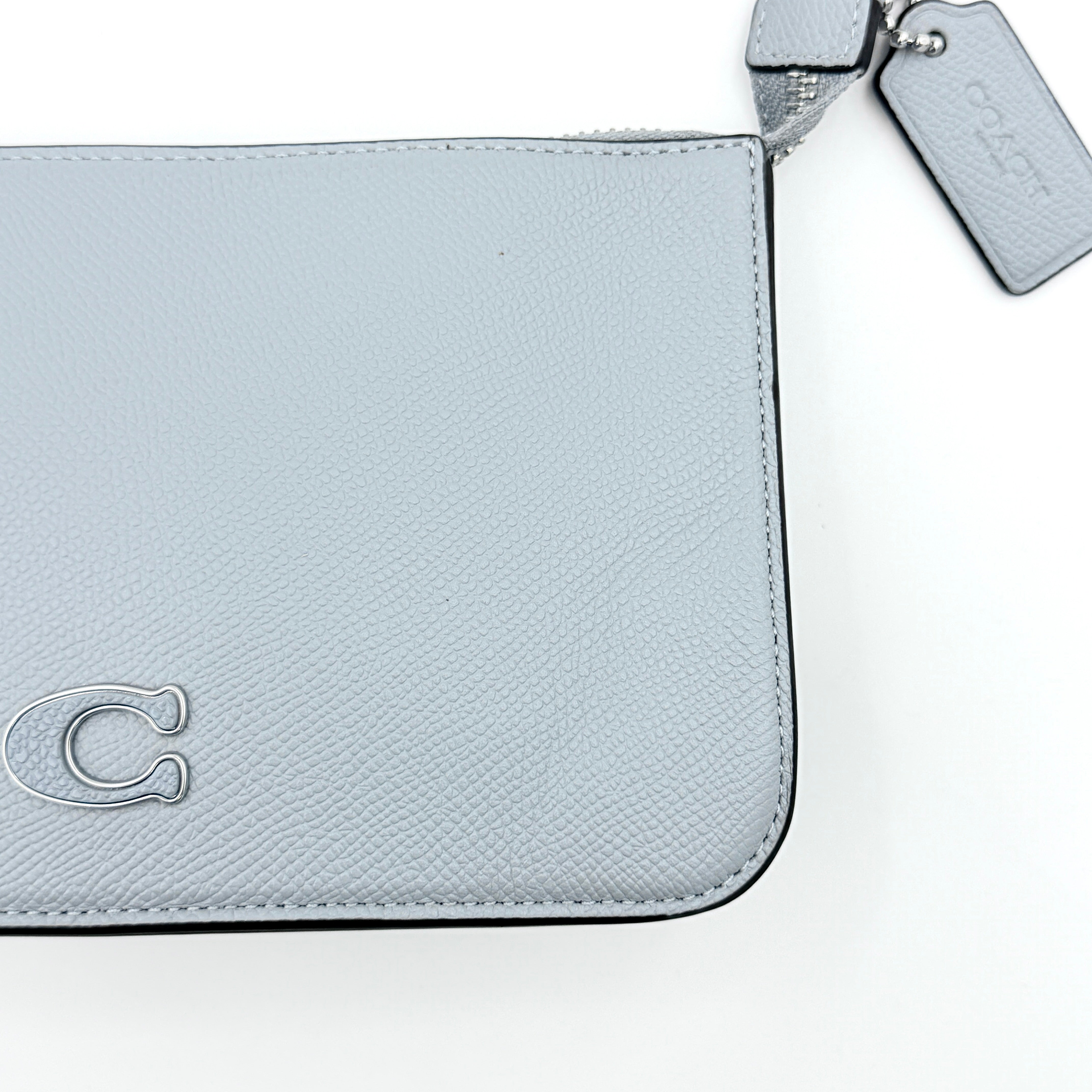 Sky blue Coach grained leather shoulder bag with silver-tone C plaque and short strap, displayed against a white background.