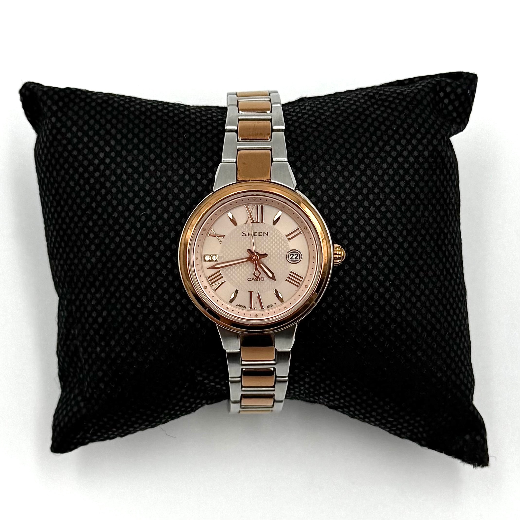 Casio Sheen SHE-4516 stainless steel watch with a rose gold and silver bracelet displayed on a black cushion.