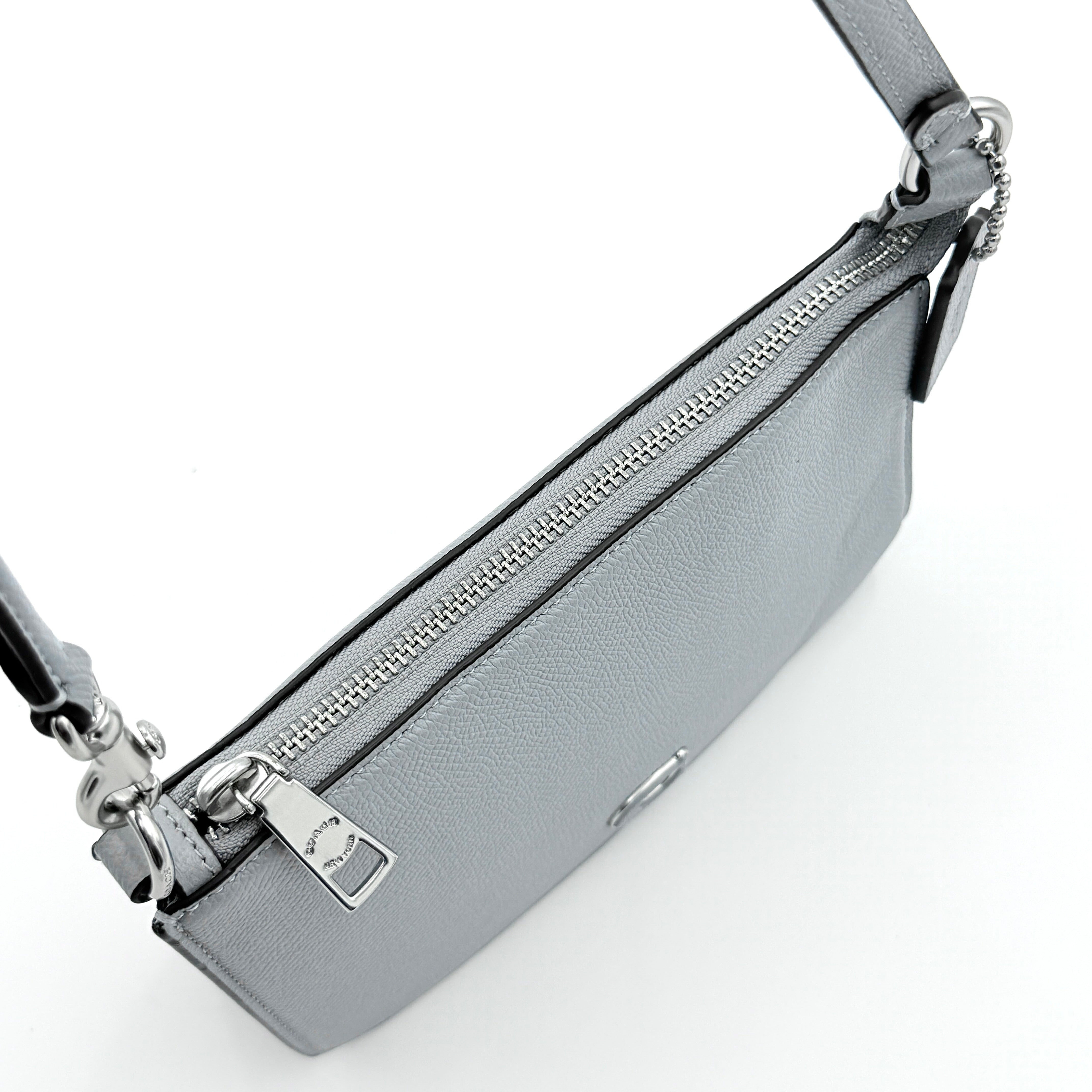 Sky blue Coach grained leather shoulder bag with silver-tone C plaque and short strap, displayed against a white background.