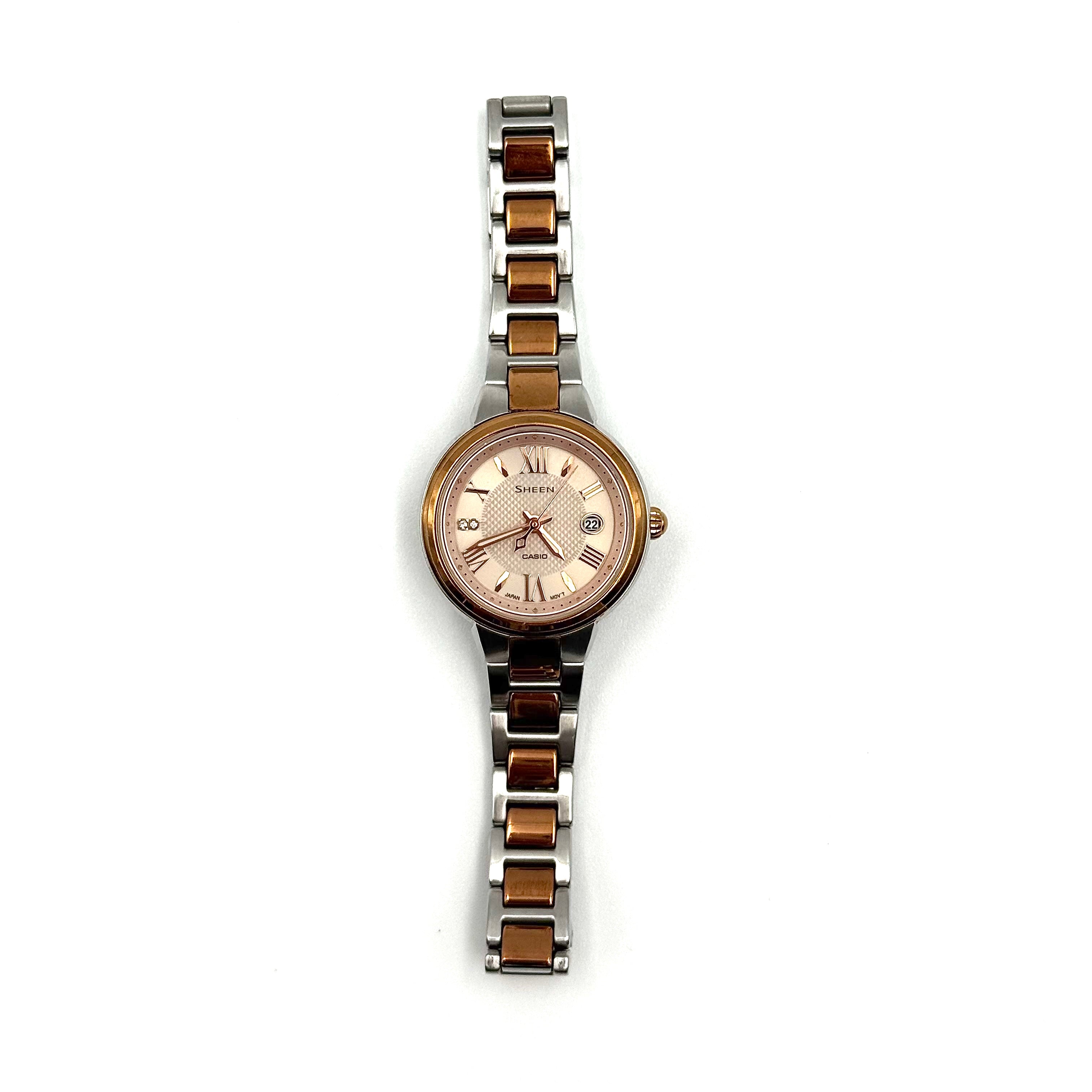Casio Sheen SHE-4516 stainless steel watch with a rose gold and silver bracelet displayed on a black cushion.