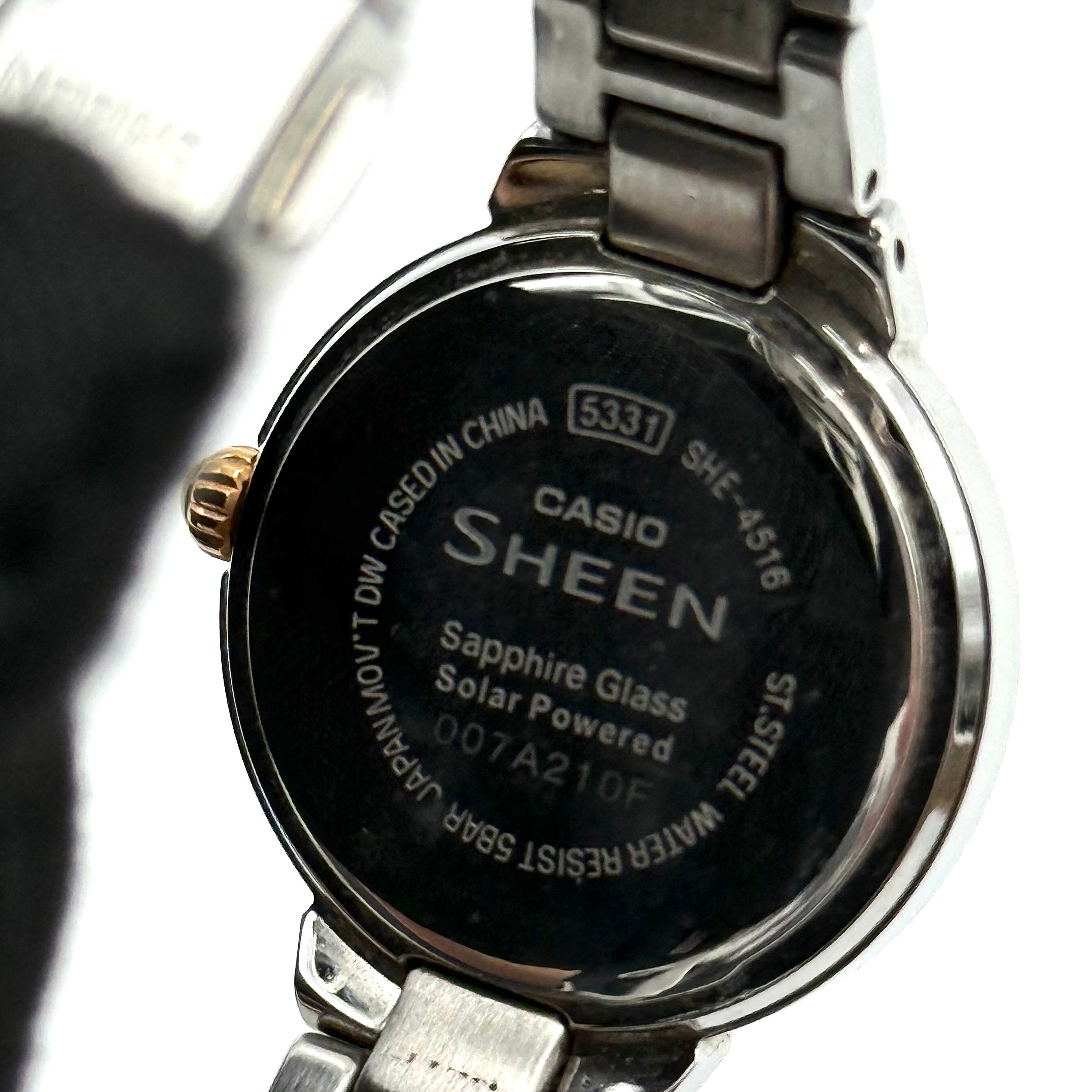 Casio Sheen SHE-4516 stainless steel watch with a rose gold and silver bracelet displayed on a black cushion.
