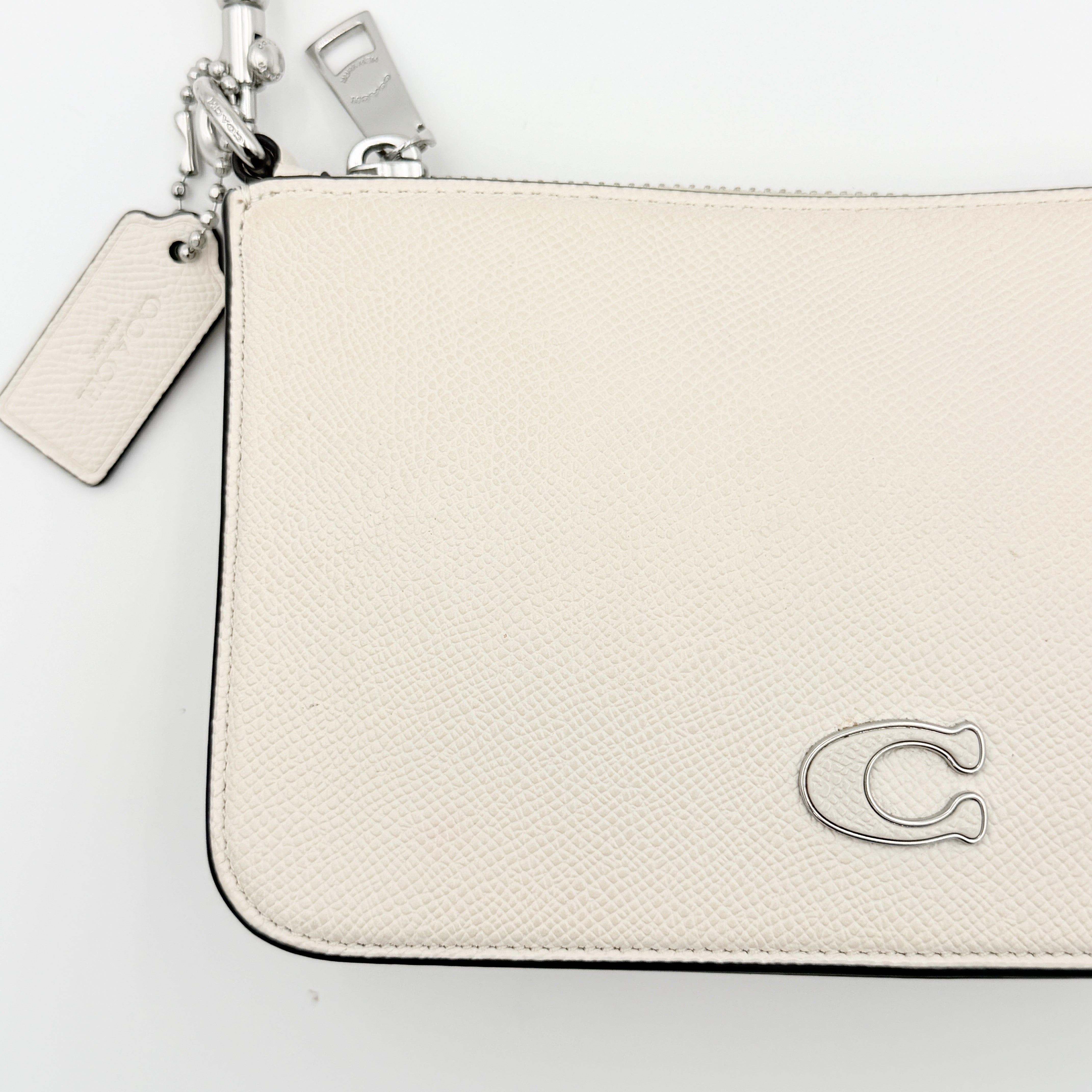 Coach cream grained leather shoulder bag with silver logo plaque and structured handle, displayed against a white background.