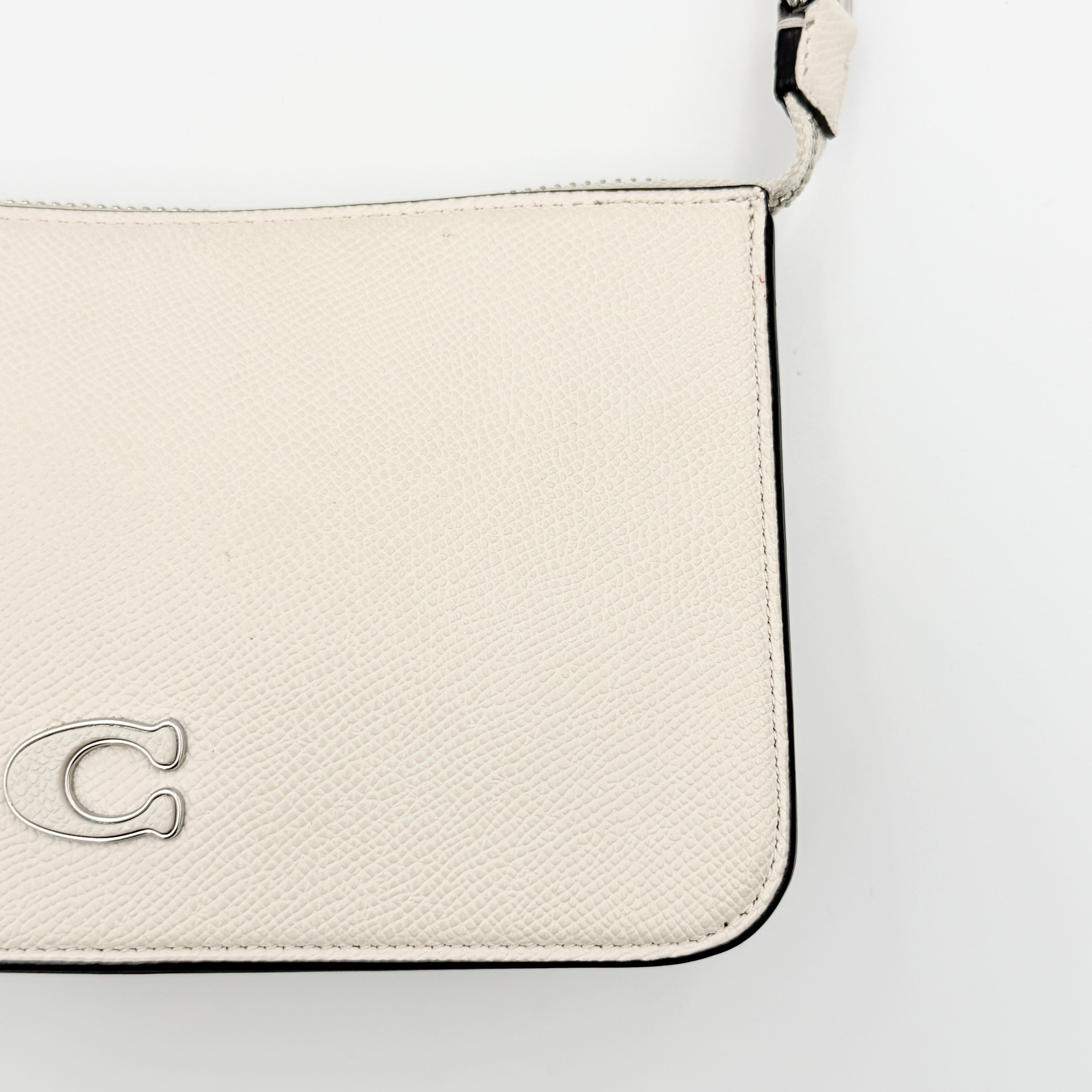 Coach cream grained leather shoulder bag with silver logo plaque and structured handle, displayed against a white background.