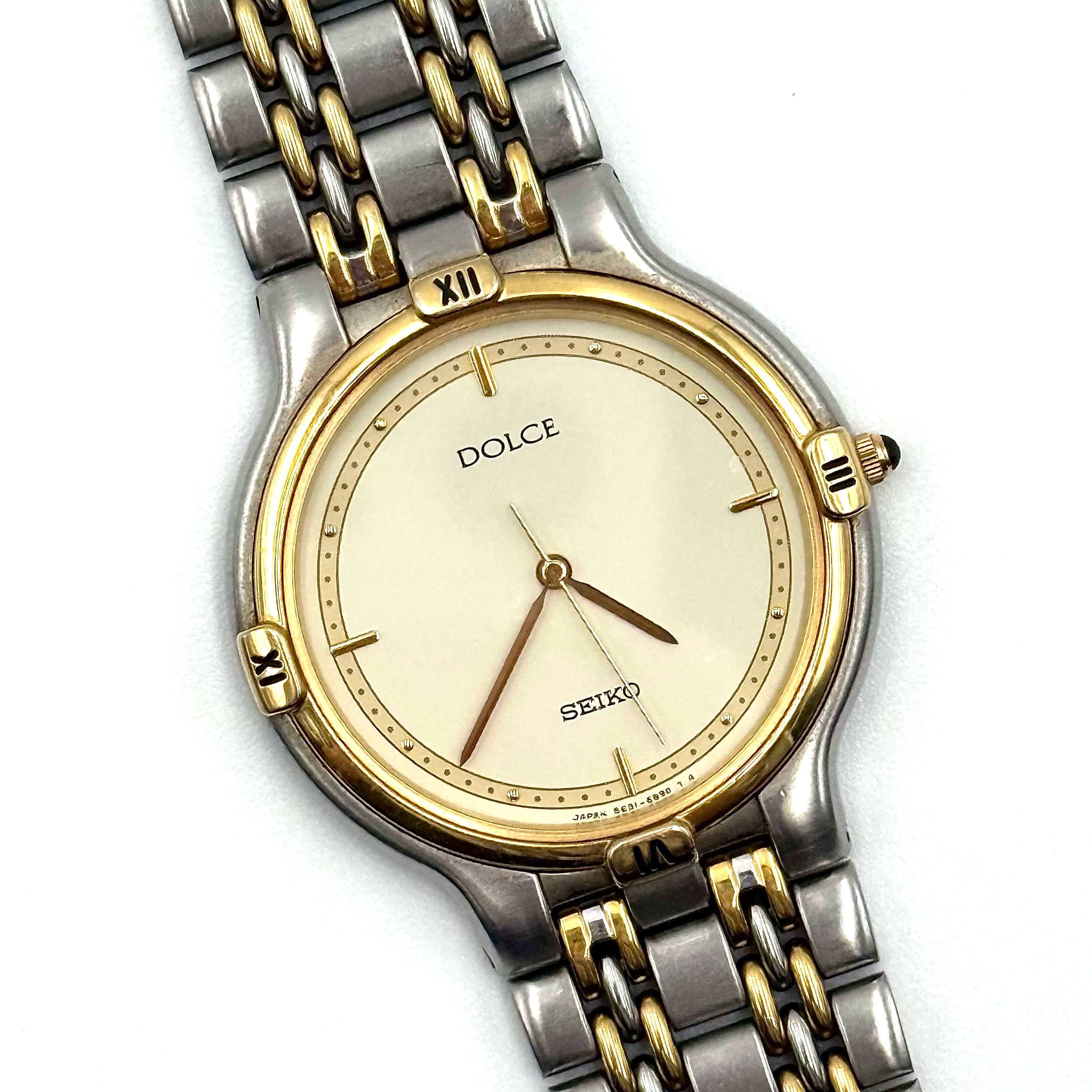Seiko Dolce 5E31-6B90 watch in stainless steel with gold-tone accents and a cream dial, displayed on a black cushion.