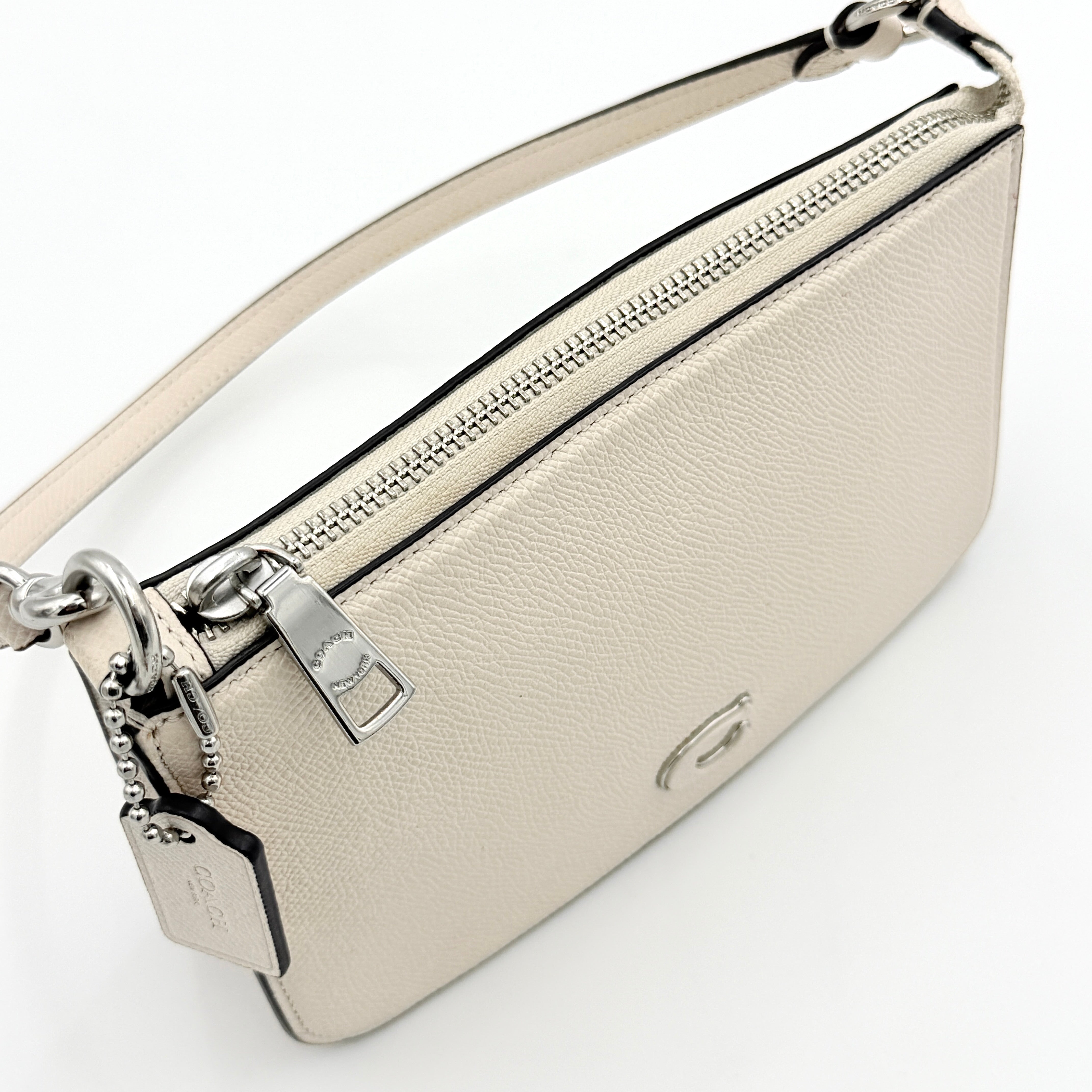 Coach cream grained leather shoulder bag with silver logo plaque and structured handle, displayed against a white background.