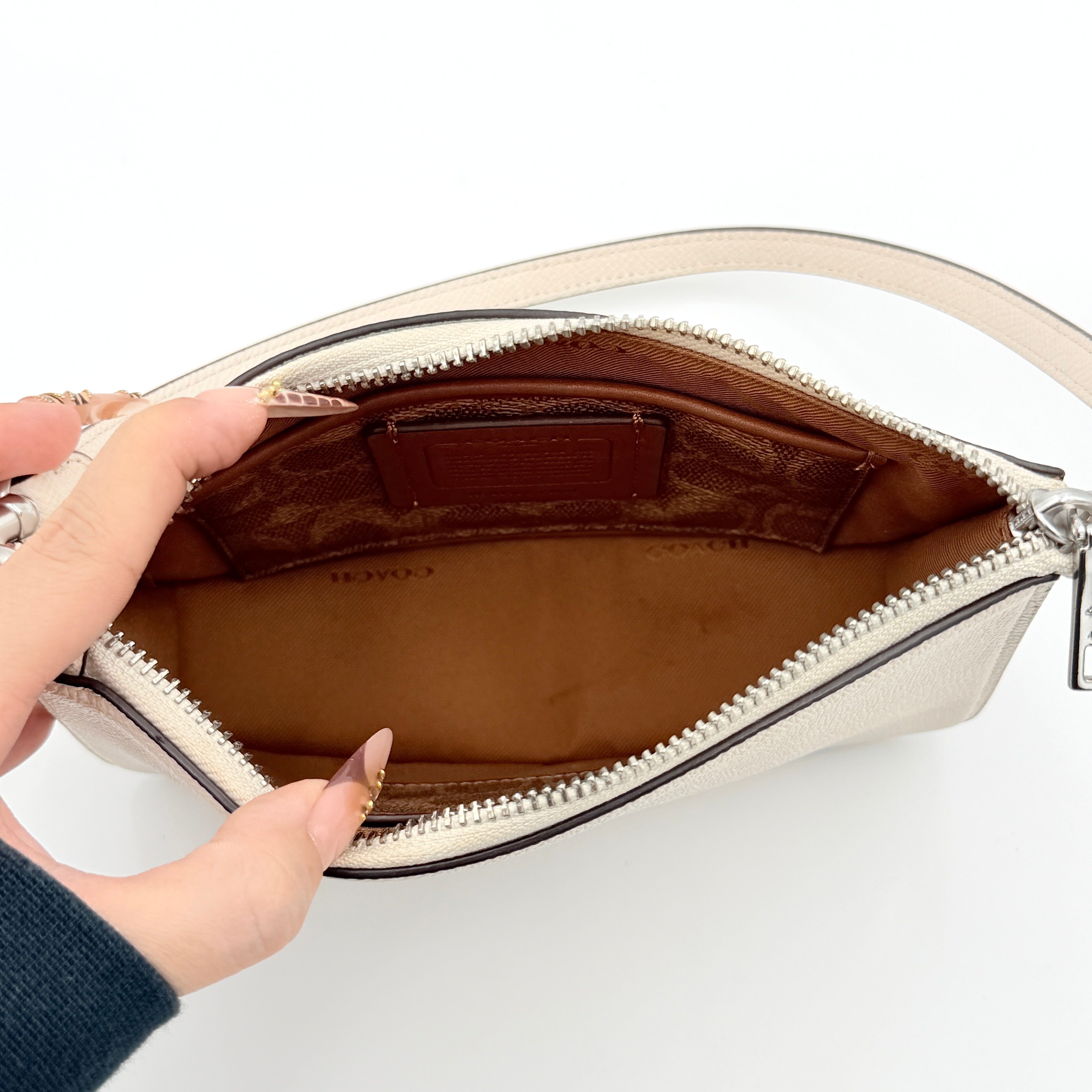 Coach cream grained leather shoulder bag with silver logo plaque and structured handle, displayed against a white background.