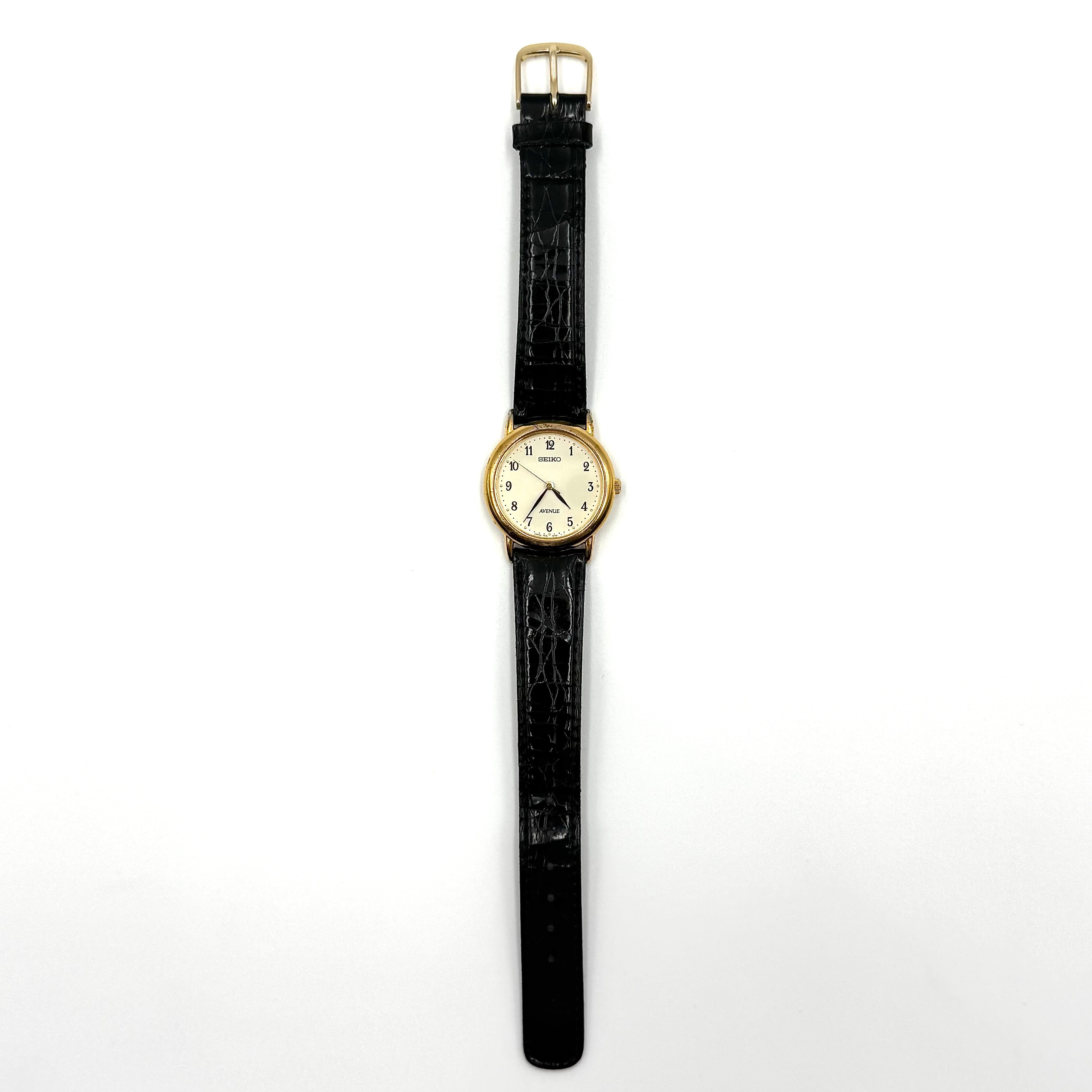 Seiko Avenue 7N01-6D50 gold watch with black textured leather strap displayed on a black cushion.