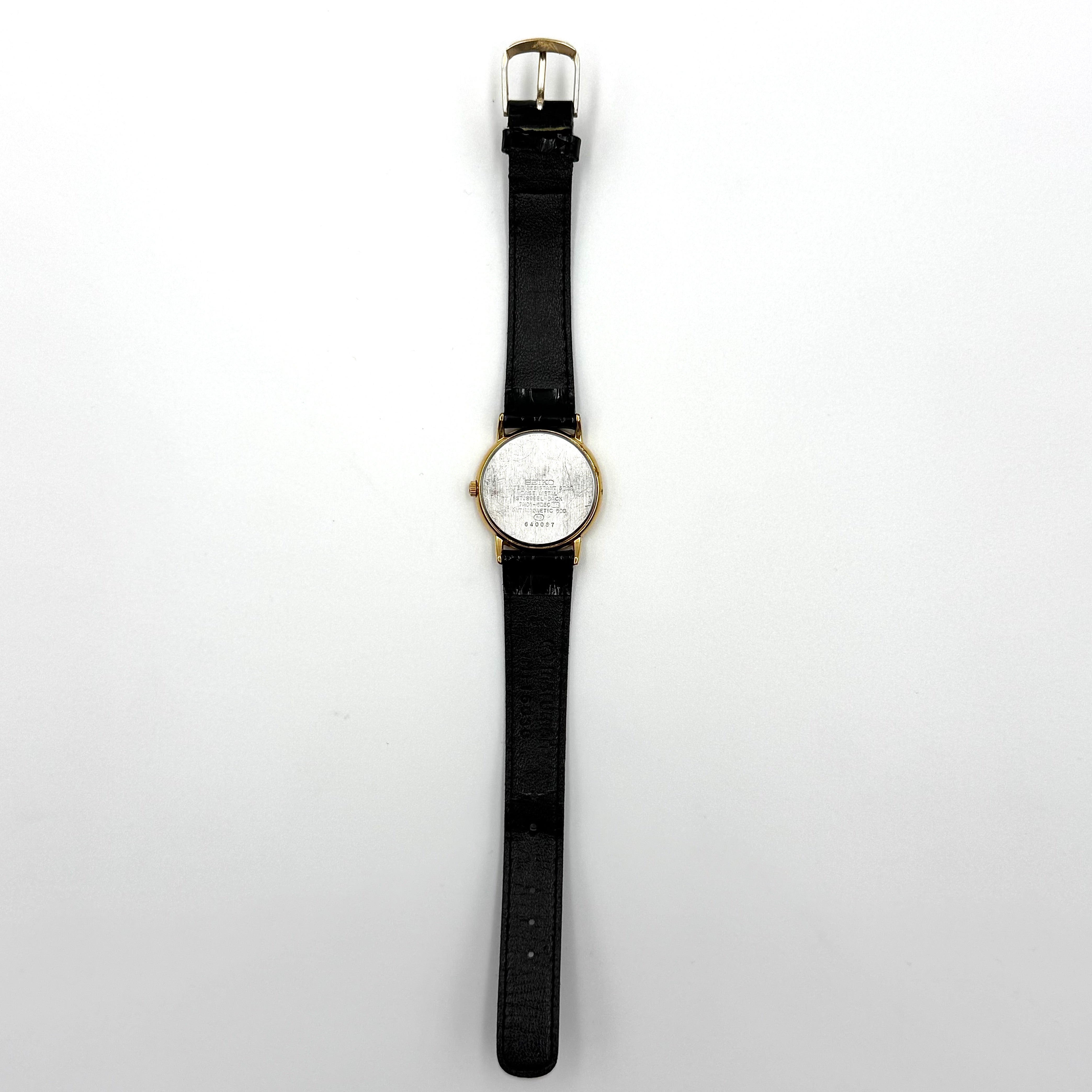 Seiko Avenue 7N01-6D50 gold watch with black textured leather strap displayed on a black cushion.