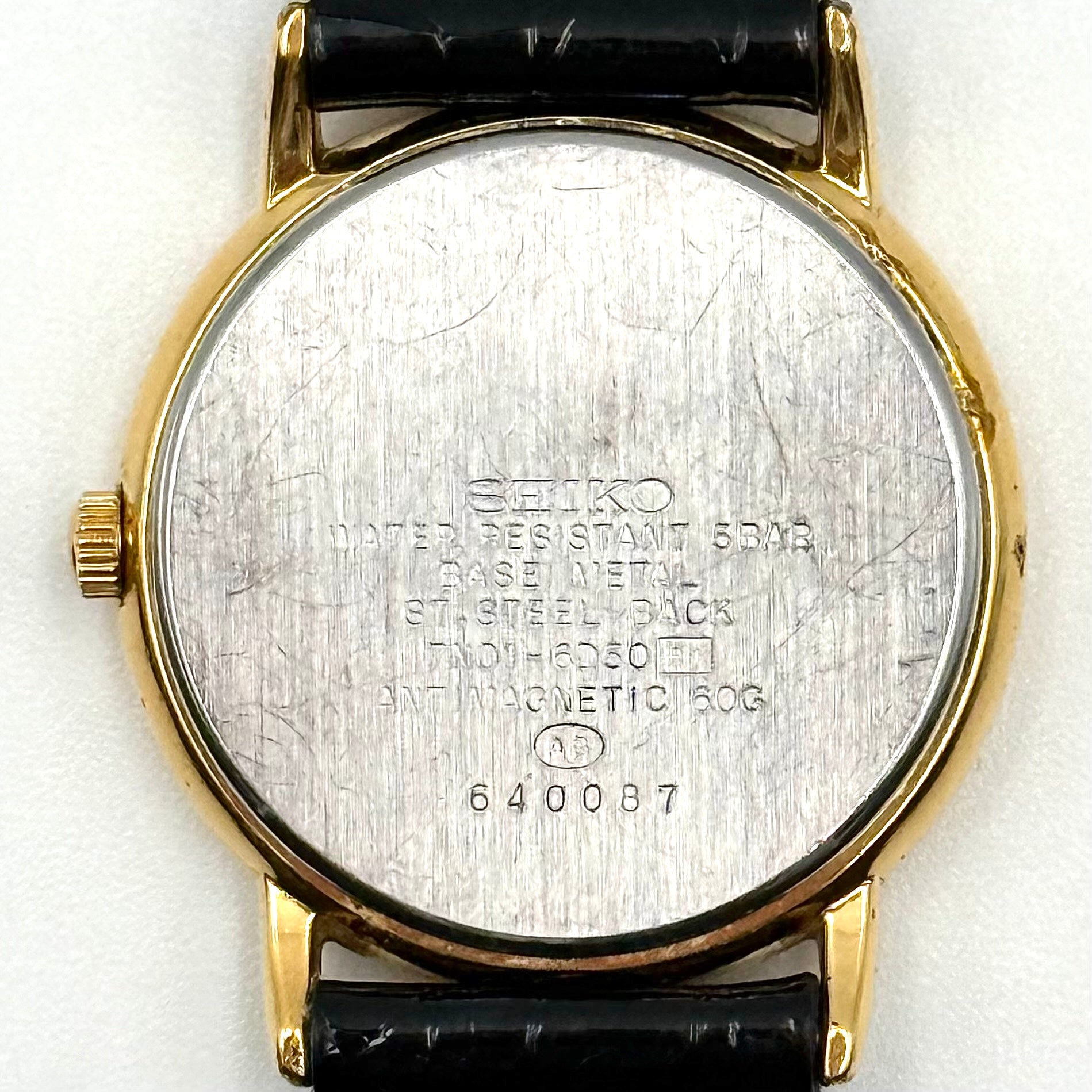 Seiko Avenue 7N01-6D50 gold watch with black textured leather strap displayed on a black cushion.
