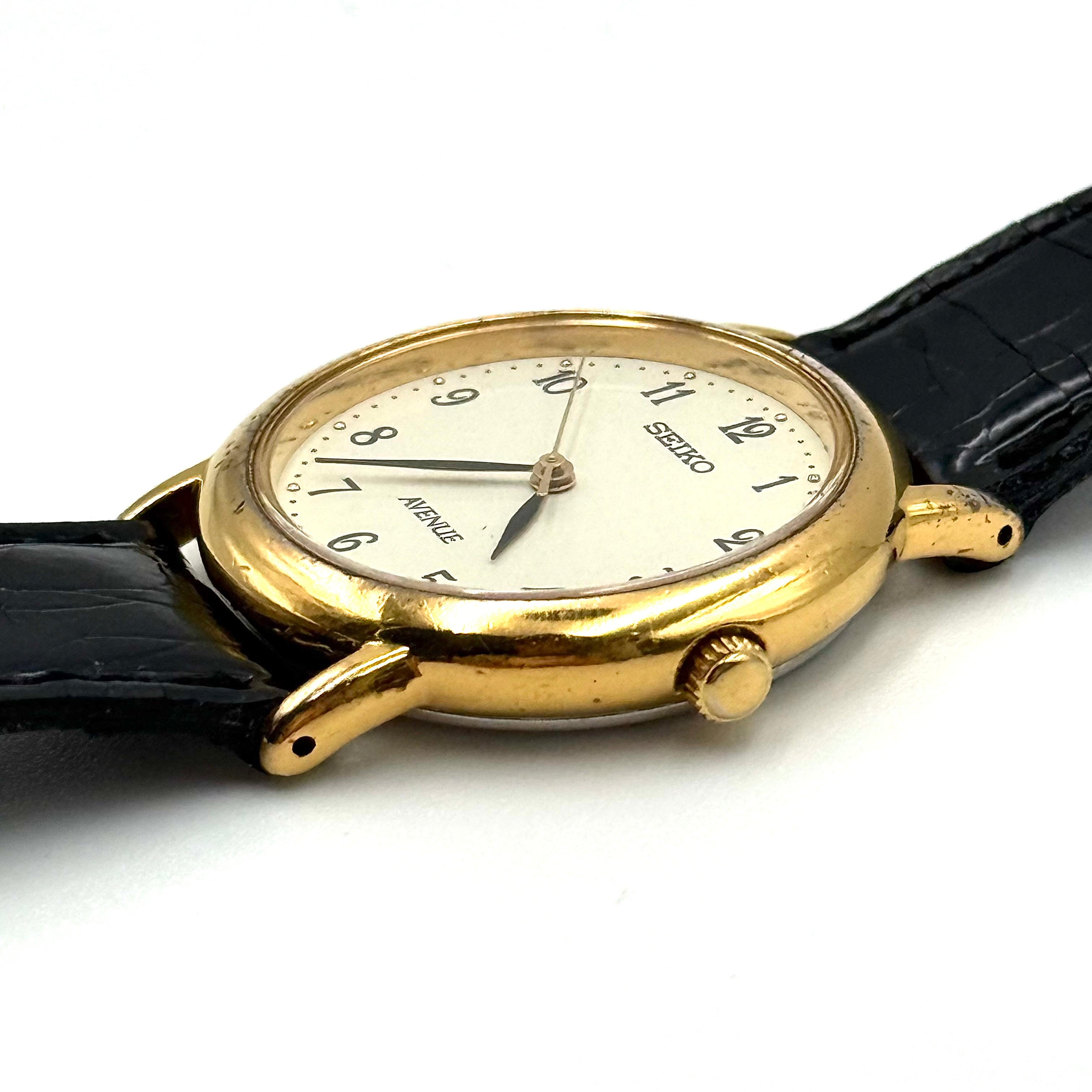 Seiko Avenue 7N01-6D50 gold watch with black textured leather strap displayed on a black cushion.