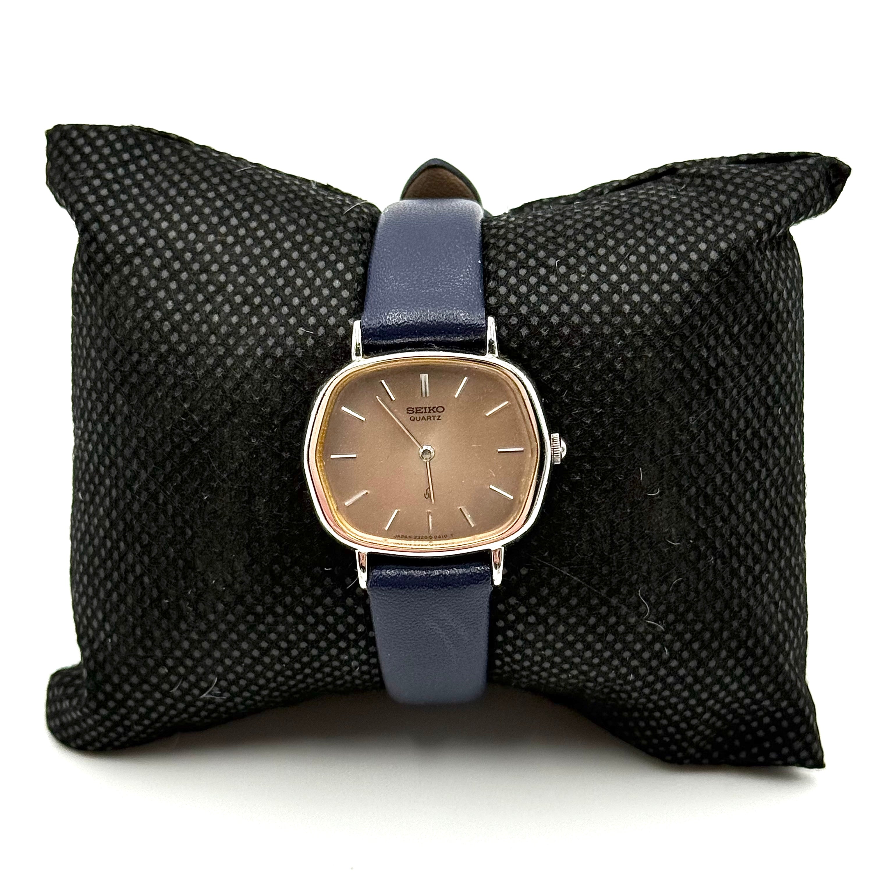 Seiko Quartz 2320-5270 with a square stainless steel case, copper dial, and navy blue leather strap displayed on a textured cushion.