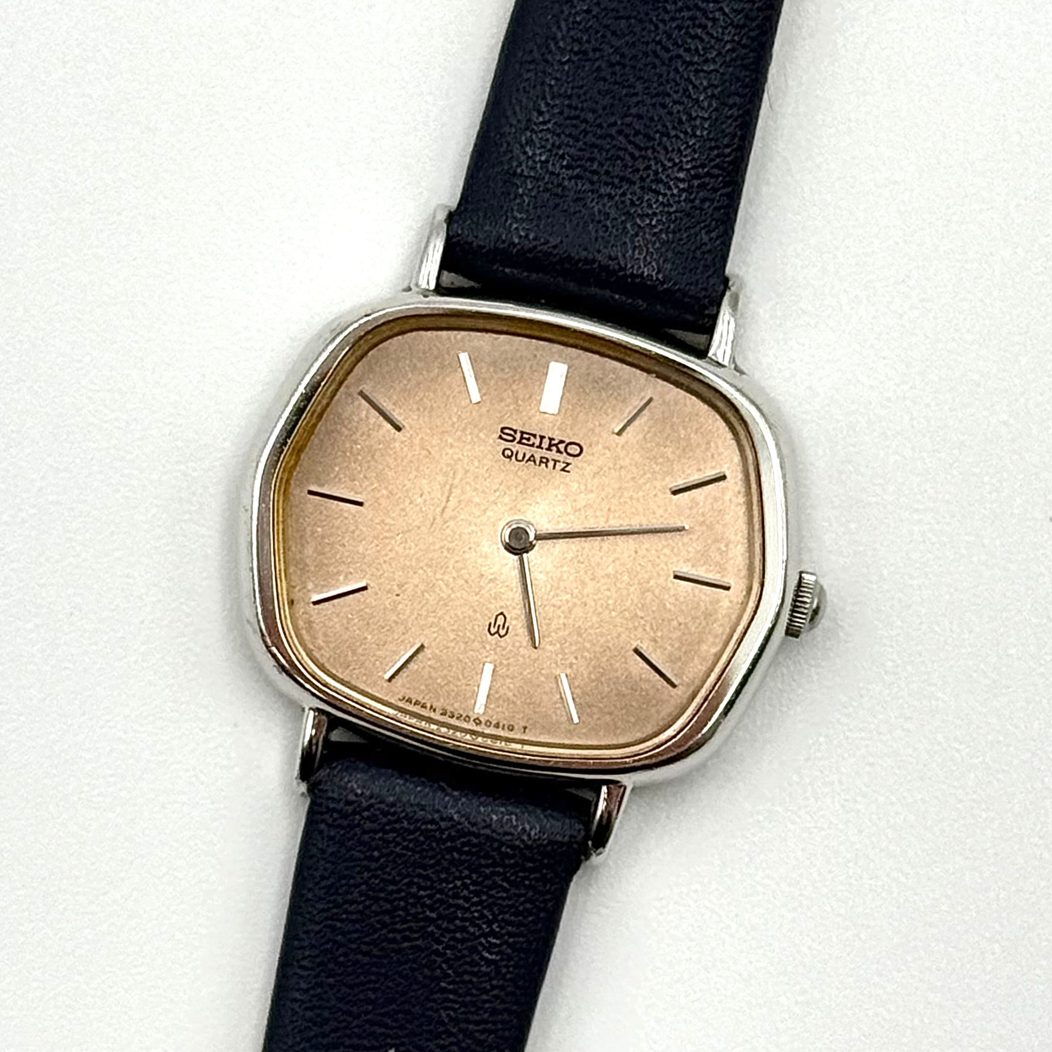 Seiko Quartz 2320-5270 with a square stainless steel case, copper dial, and navy blue leather strap displayed on a textured cushion.