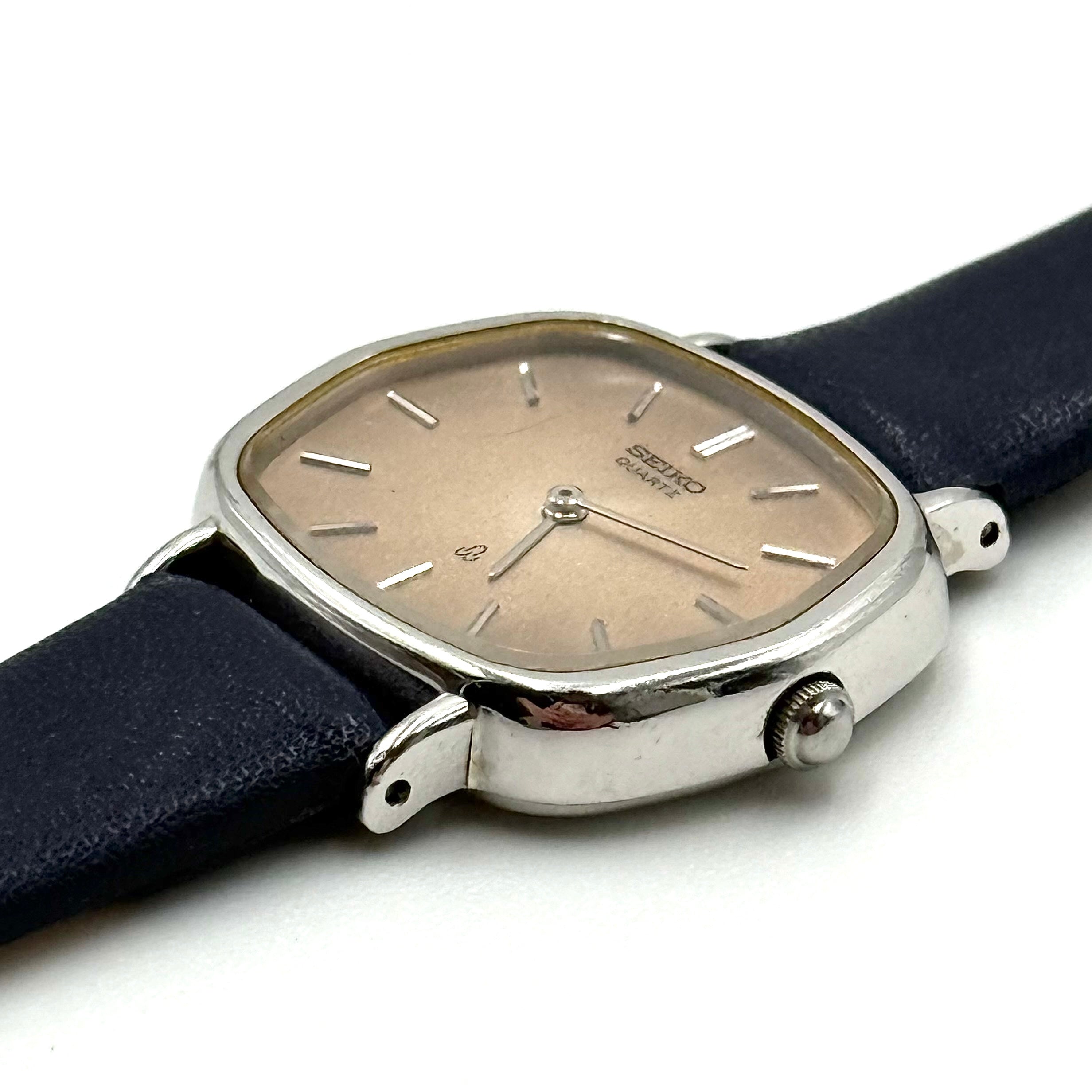 Seiko Quartz 2320-5270 with a square stainless steel case, copper dial, and navy blue leather strap displayed on a textured cushion.
