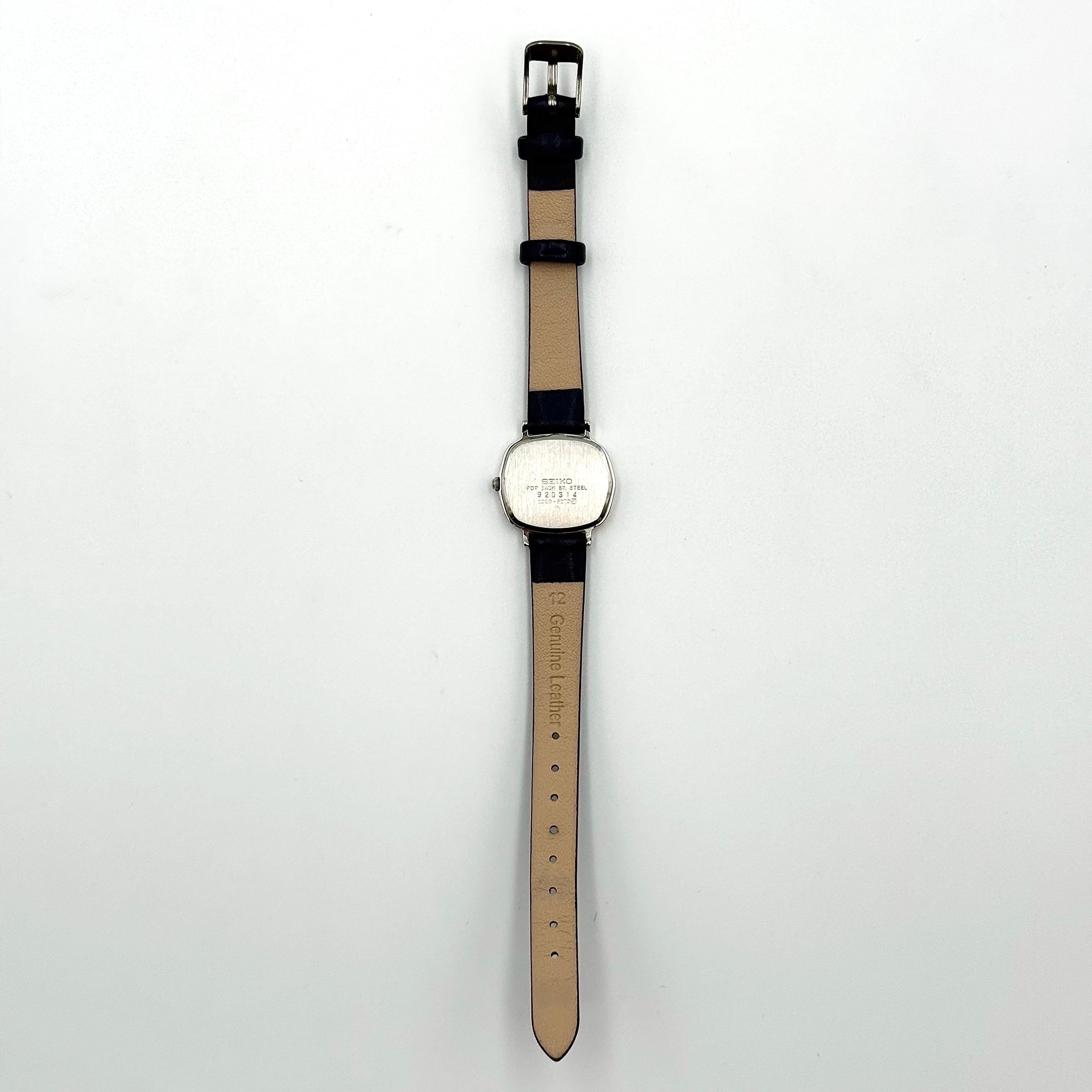 Seiko Quartz 2320-5270 with a square stainless steel case, copper dial, and navy blue leather strap displayed on a textured cushion.