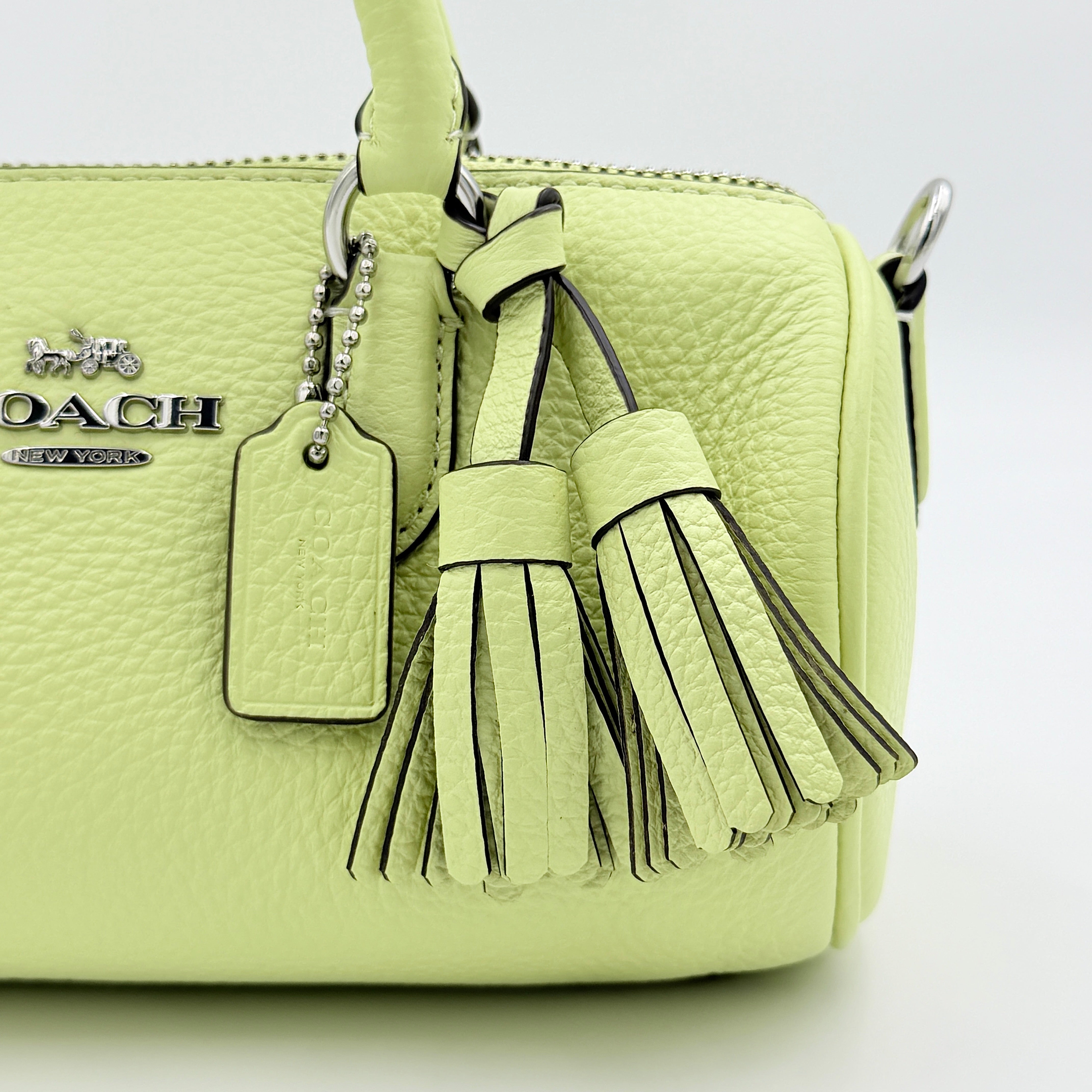 Coach 2Way Lacey Mini Boston Bag in light green pebbled leather with tassels and a detachable strap, shown against a plain background.