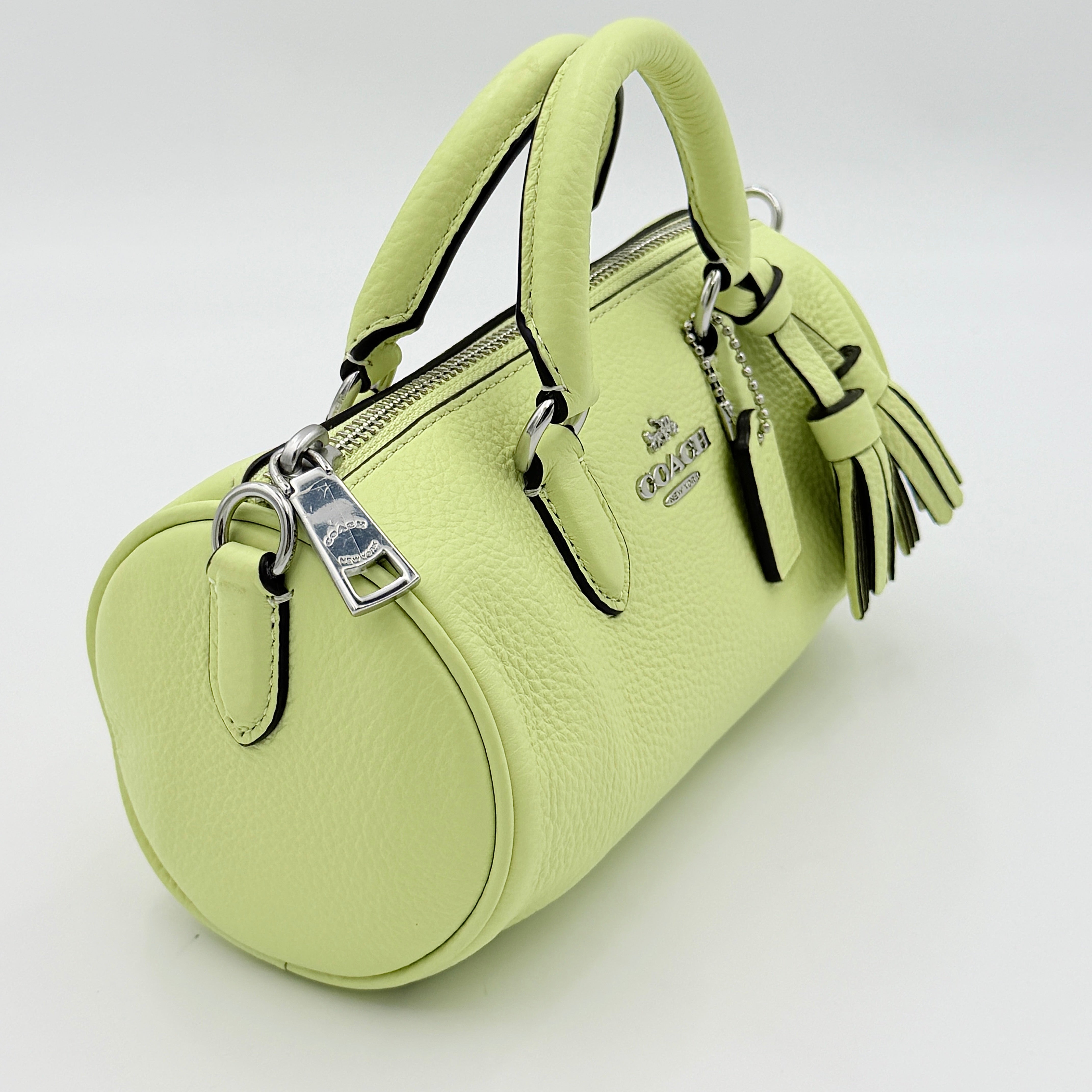 Coach 2Way Lacey Mini Boston Bag in light green pebbled leather with tassels and a detachable strap, shown against a plain background.