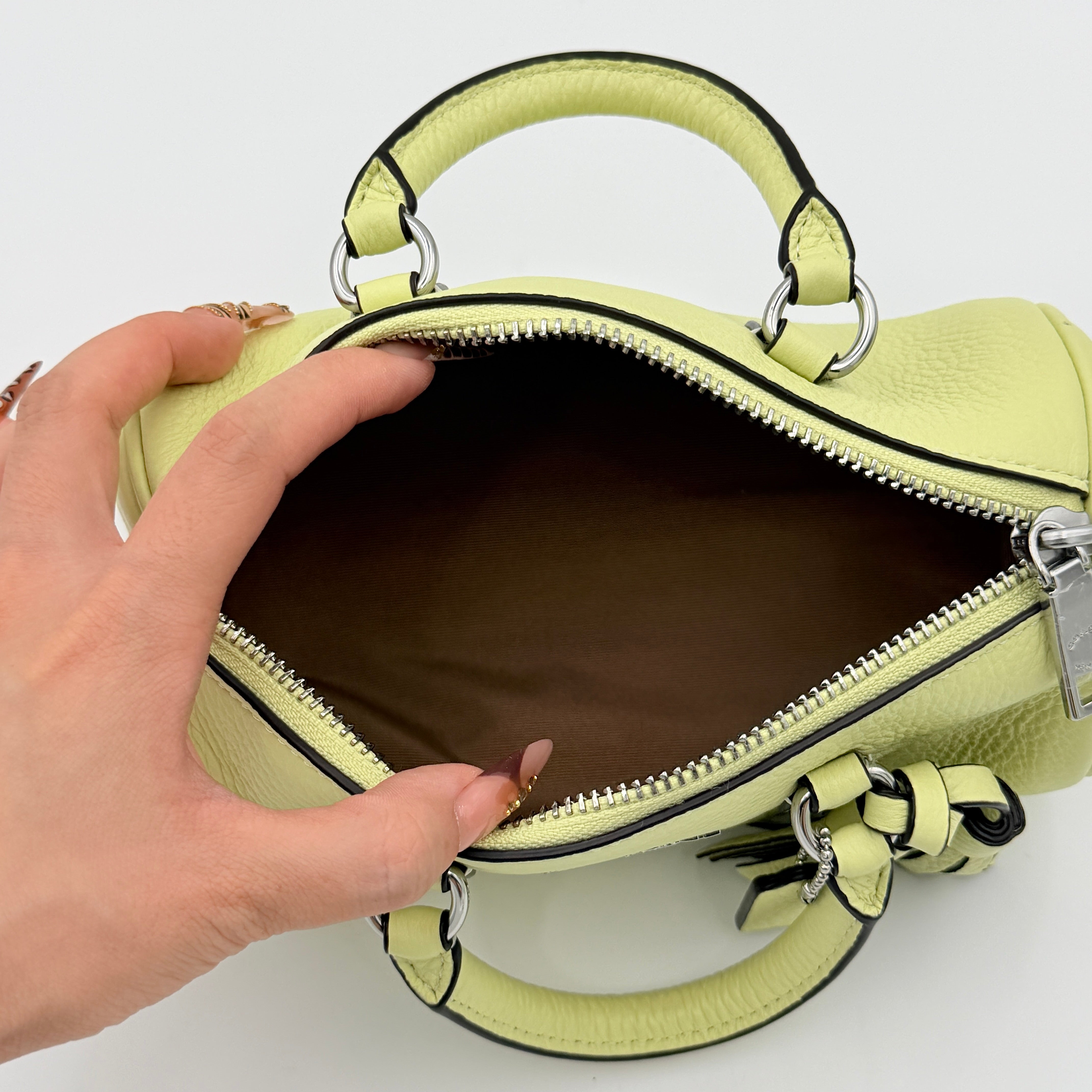 Coach 2Way Lacey Mini Boston Bag in light green pebbled leather with tassels and a detachable strap, shown against a plain background.