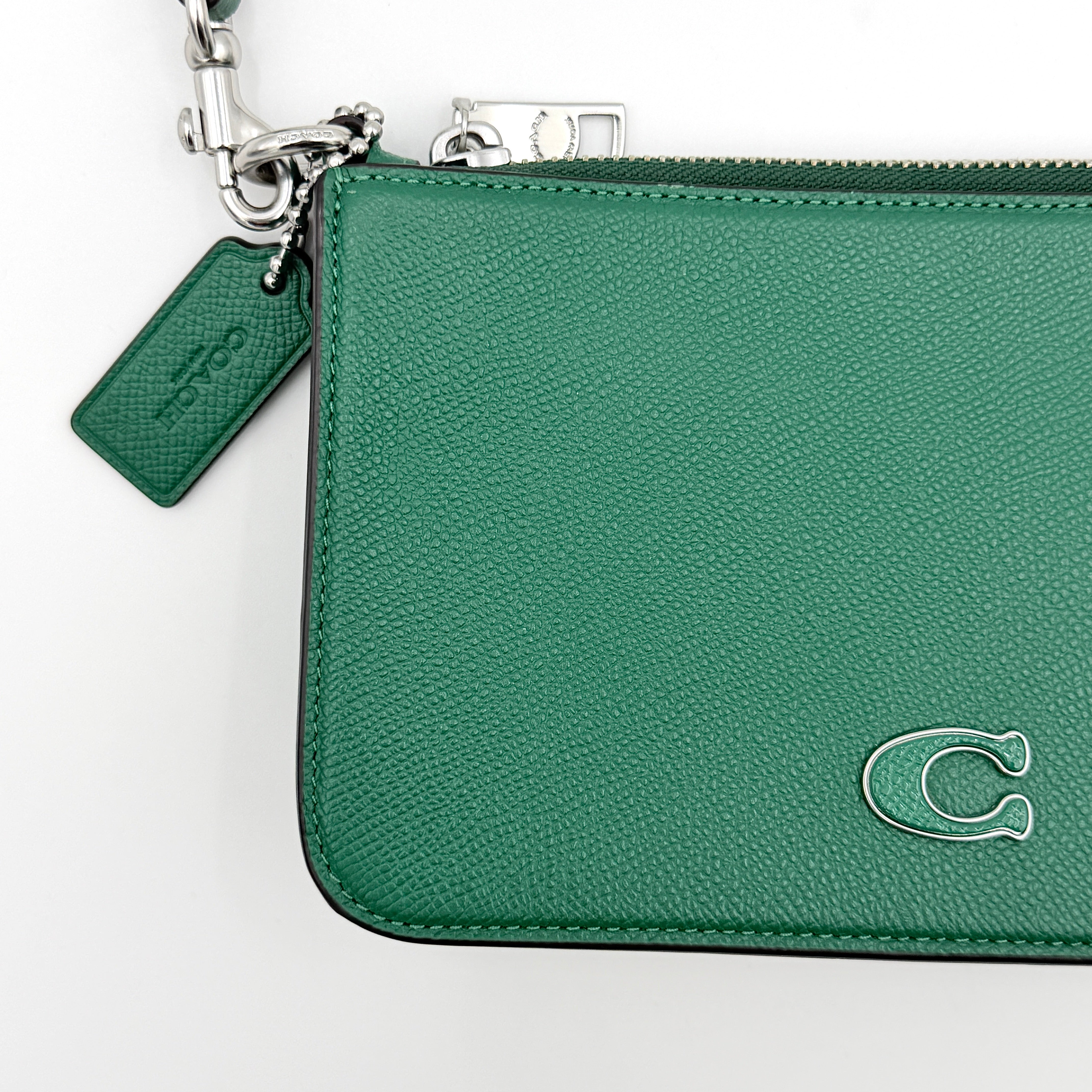 Coach green grained leather shoulder bag with silver C plaque and top zip, styled with a short strap.