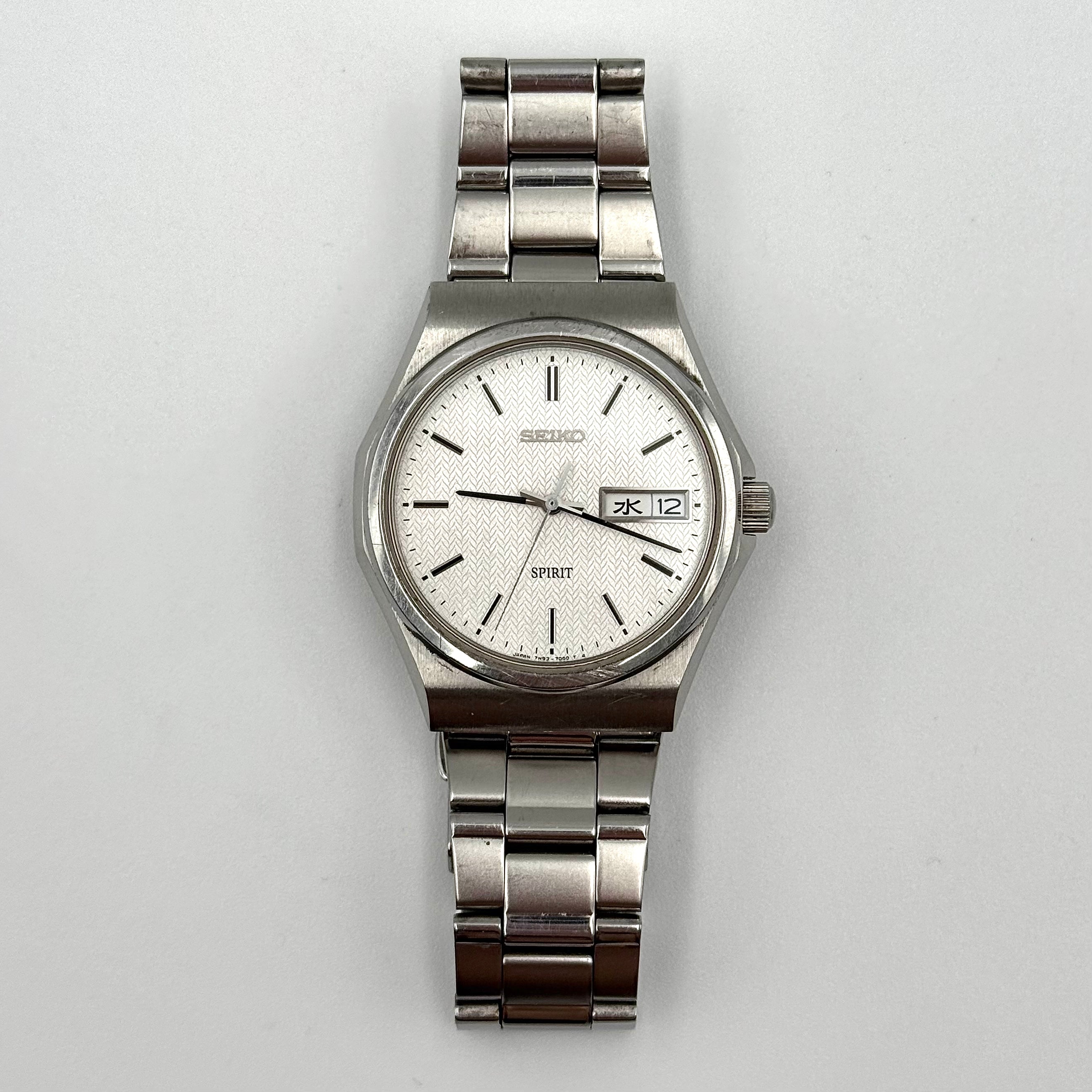 Seiko Spirit 7N93-7000 Quartz Watch in silver with a white textured dial and stainless steel bracelet, shown on a black cushion.