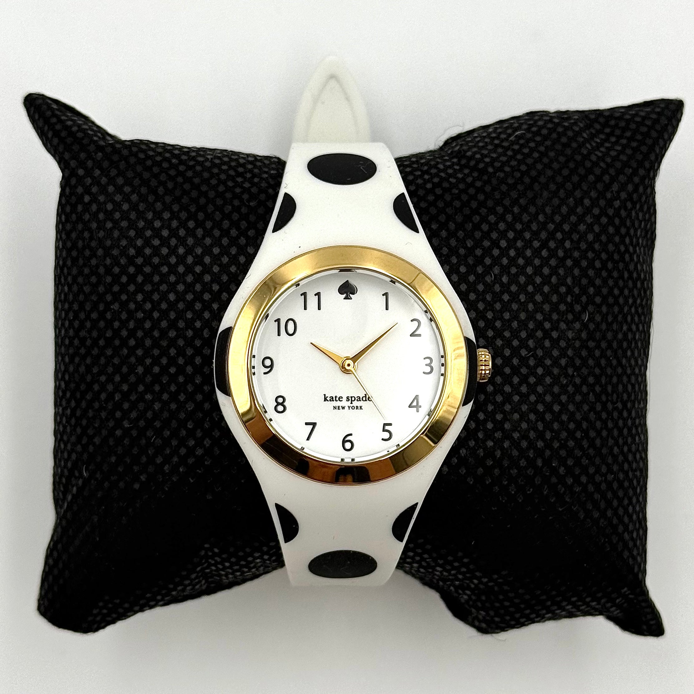 Kate Spade New York Rumsey 0838 silicone watch in white with black polka dots, gold-tone bezel, and white dial displayed on a cushion.