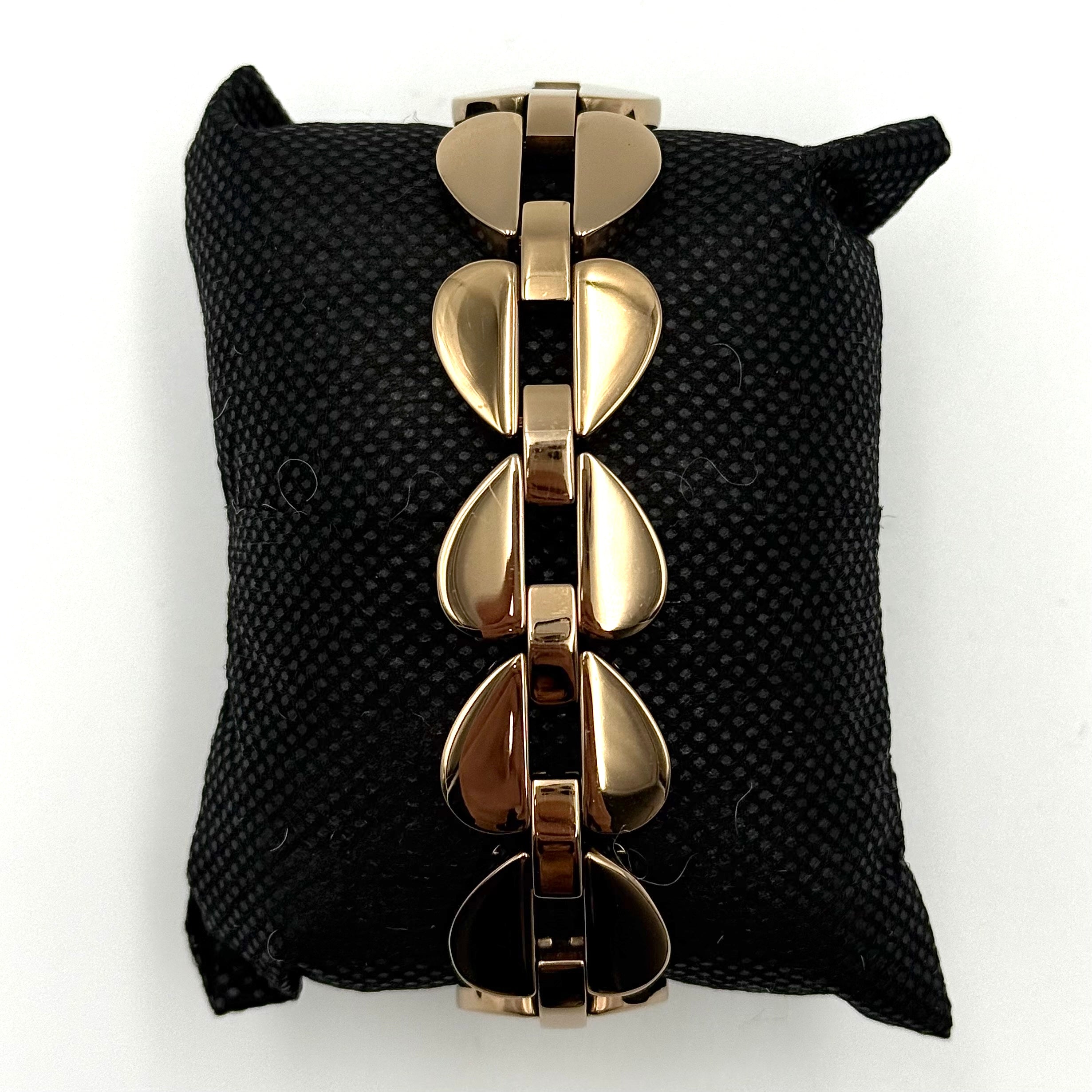 Kate Spade Annadale gold bracelet watch with white dial and heart-shaped links displayed on a black cushion.