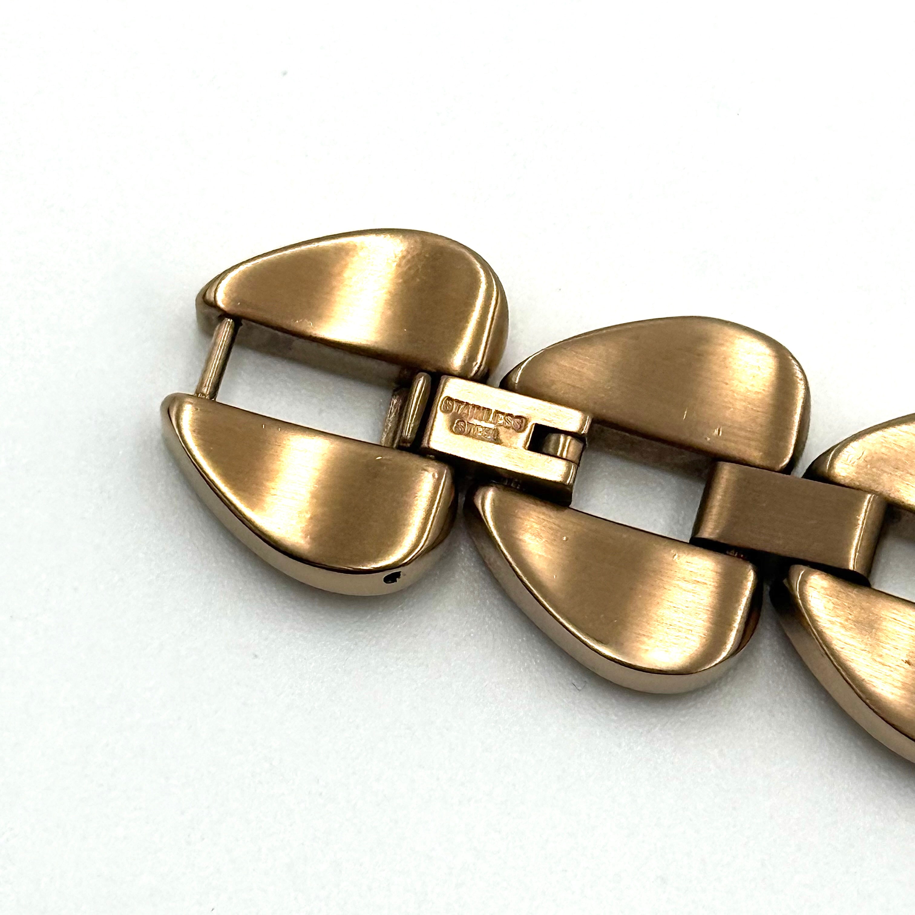 Kate Spade Annadale gold bracelet watch with white dial and heart-shaped links displayed on a black cushion.