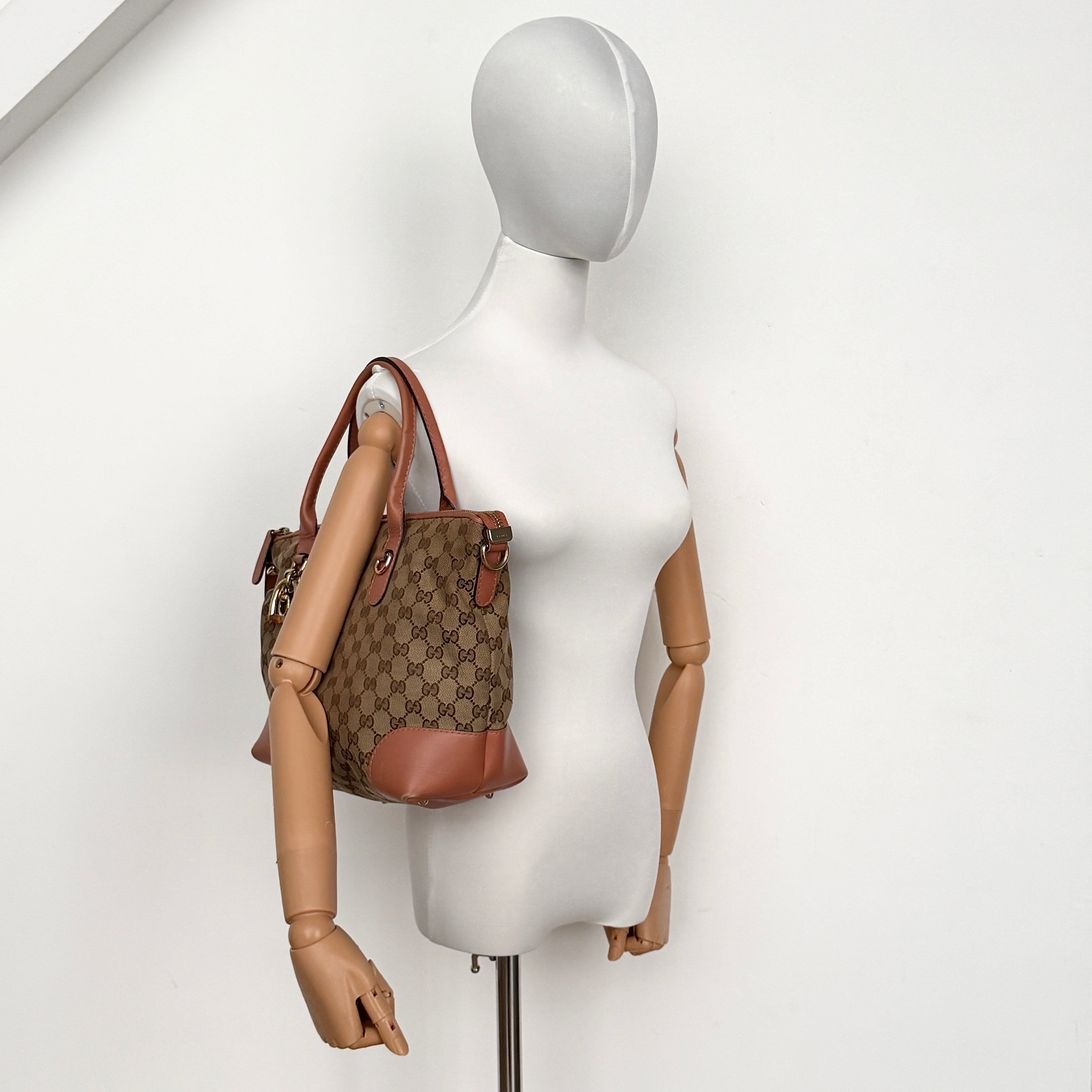 Gucci beige GG monogram shoulder bag with orange leather trim, heart bit charm, and detachable strap displayed on a white background.