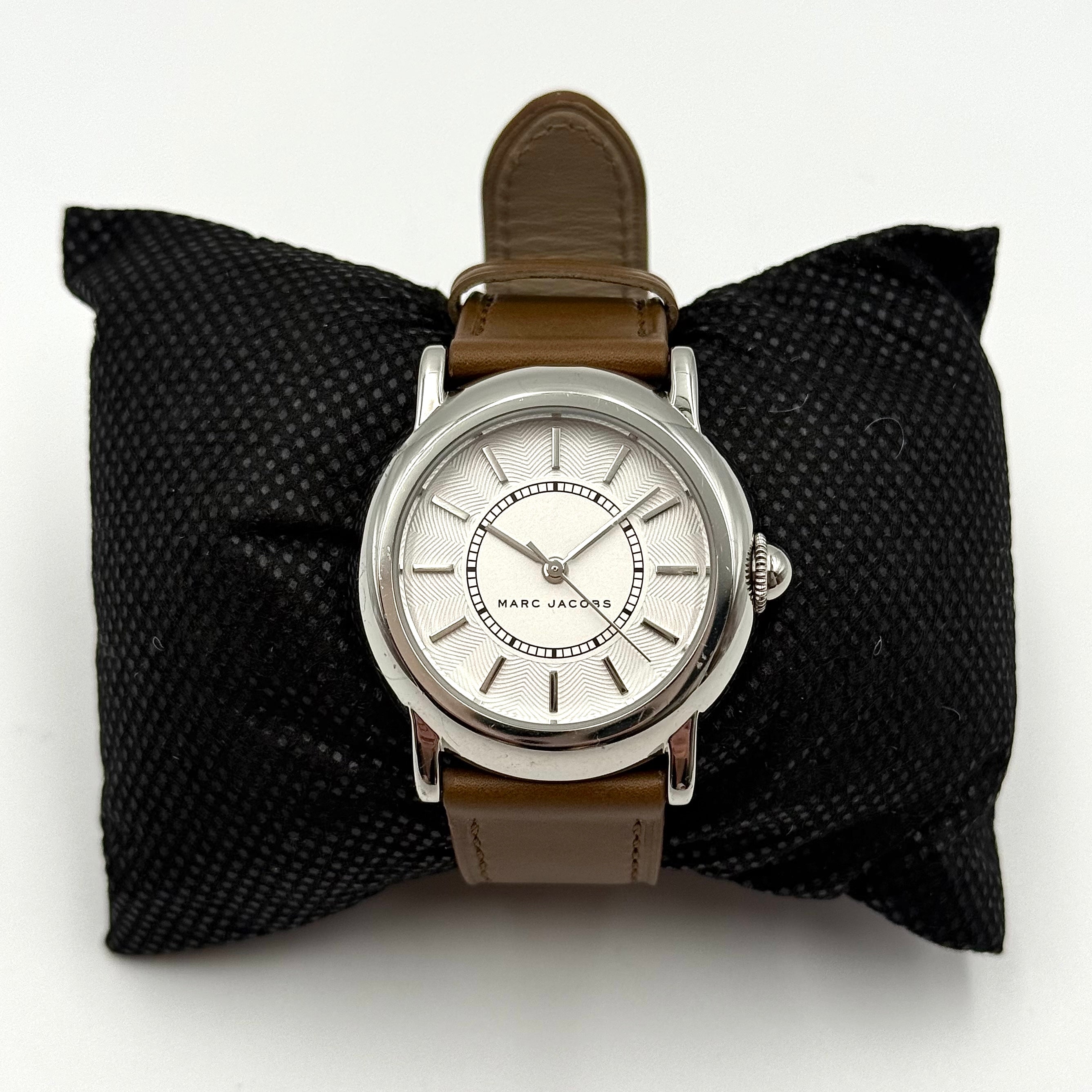 Marc Jacobs Courtney watch with silver stainless steel case and brown leather strap shown on a black cushion.