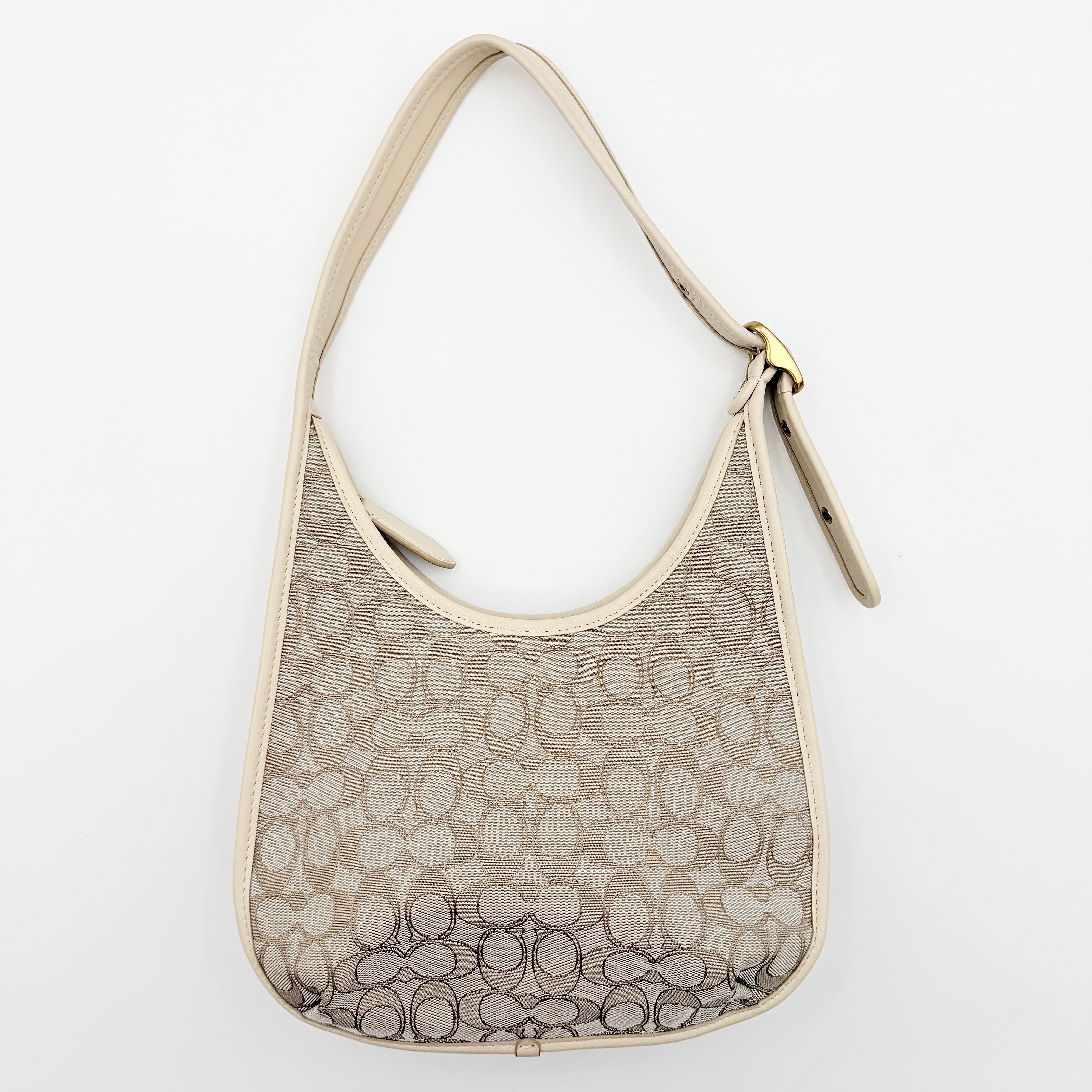 Coach Signature Ergo Shoulder Bag in beige and cream canvas with cream leather trim and brass adjustable buckle, displayed on a white background.
