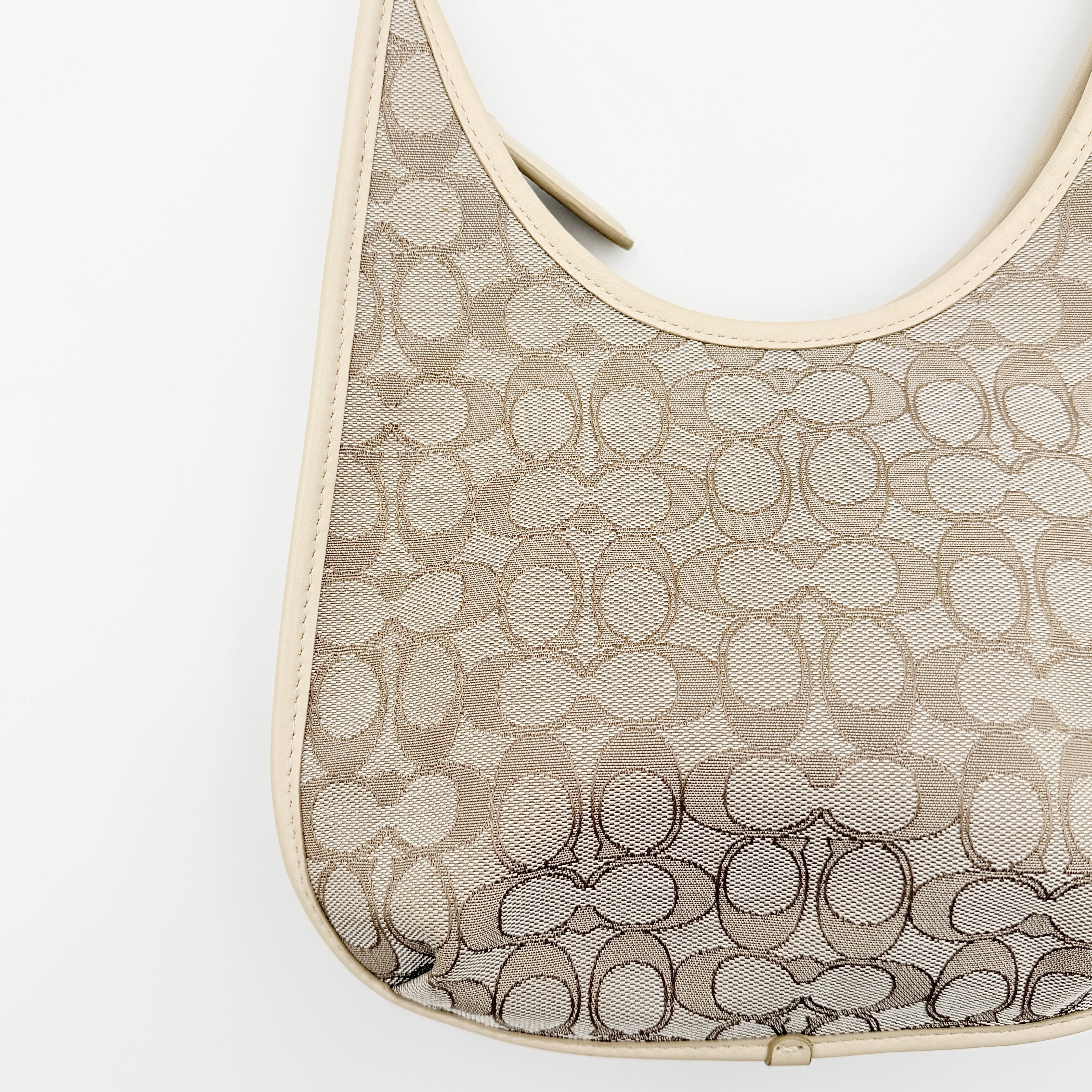Coach Signature Ergo Shoulder Bag in beige and cream canvas with cream leather trim and brass adjustable buckle, displayed on a white background.
