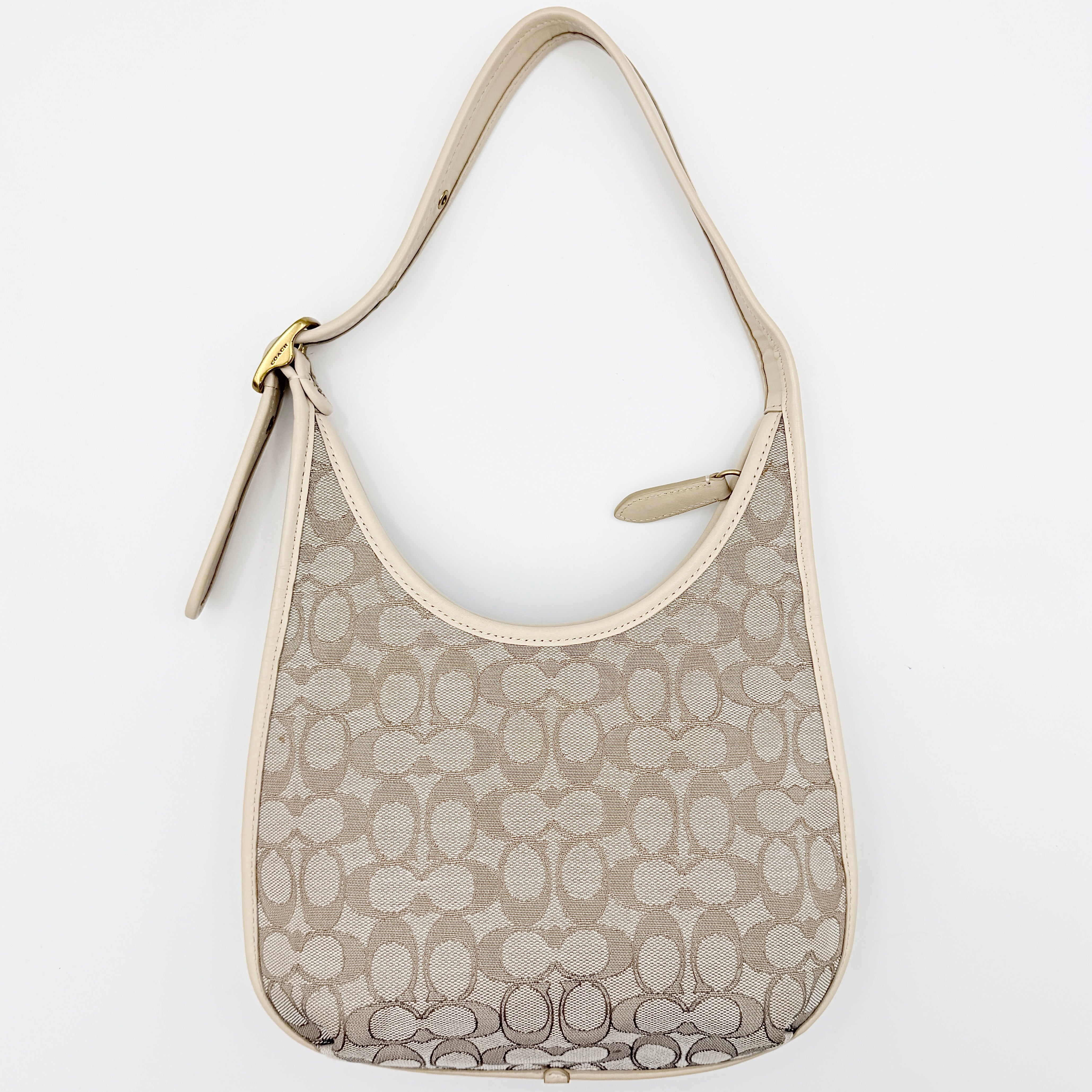 Coach Signature Ergo Shoulder Bag in beige and cream canvas with cream leather trim and brass adjustable buckle, displayed on a white background.