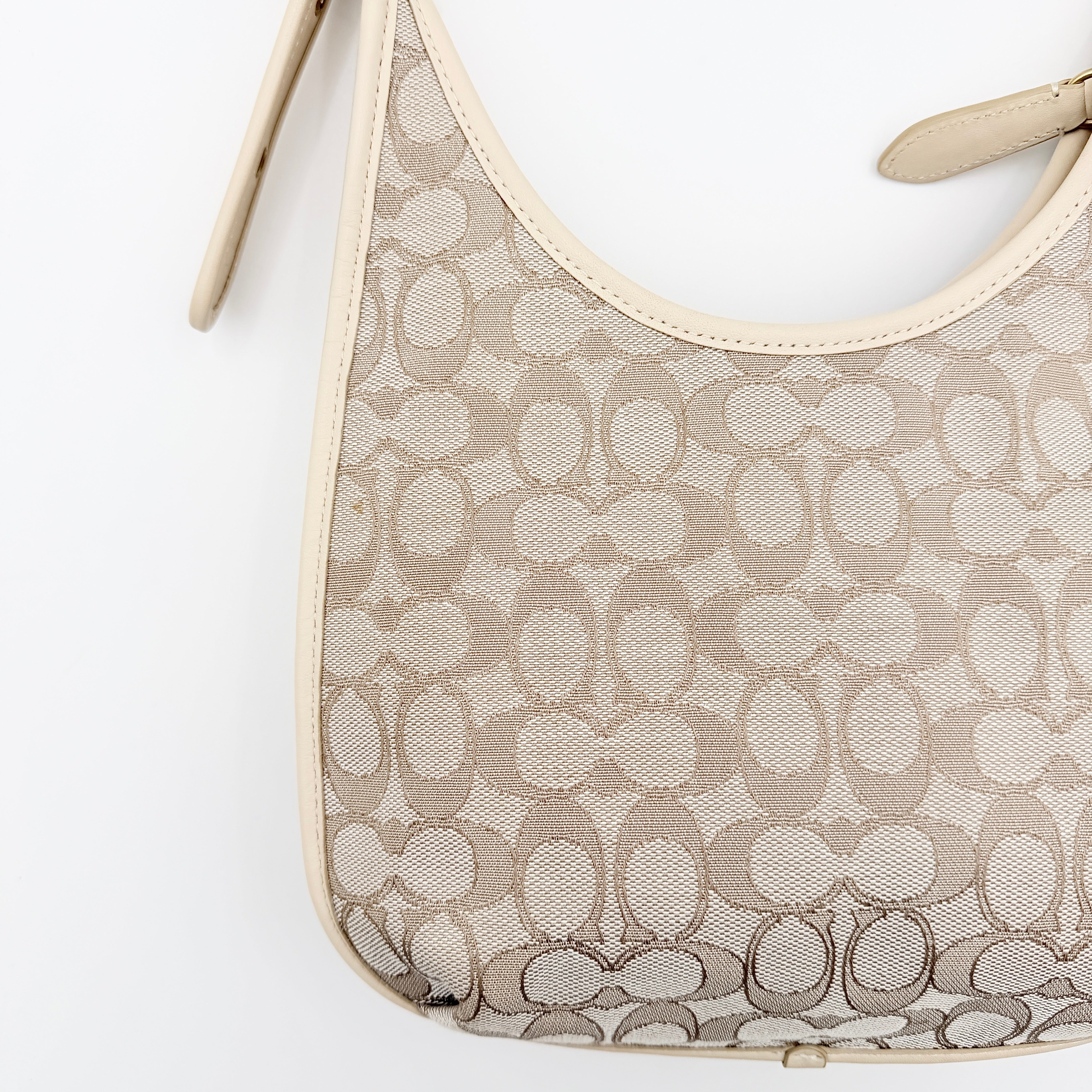 Coach Signature Ergo Shoulder Bag in beige and cream canvas with cream leather trim and brass adjustable buckle, displayed on a white background.