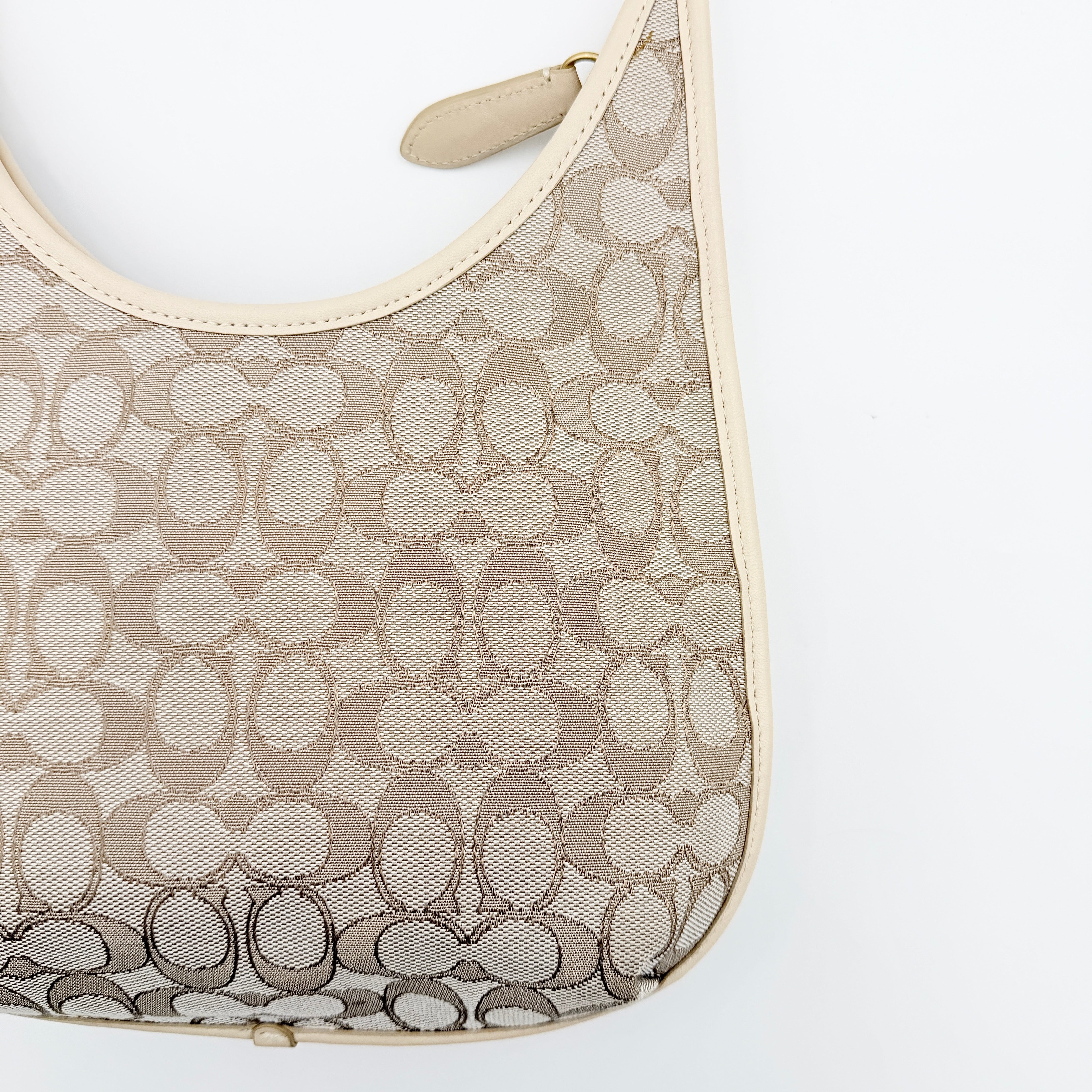 Coach Signature Ergo Shoulder Bag in beige and cream canvas with cream leather trim and brass adjustable buckle, displayed on a white background.