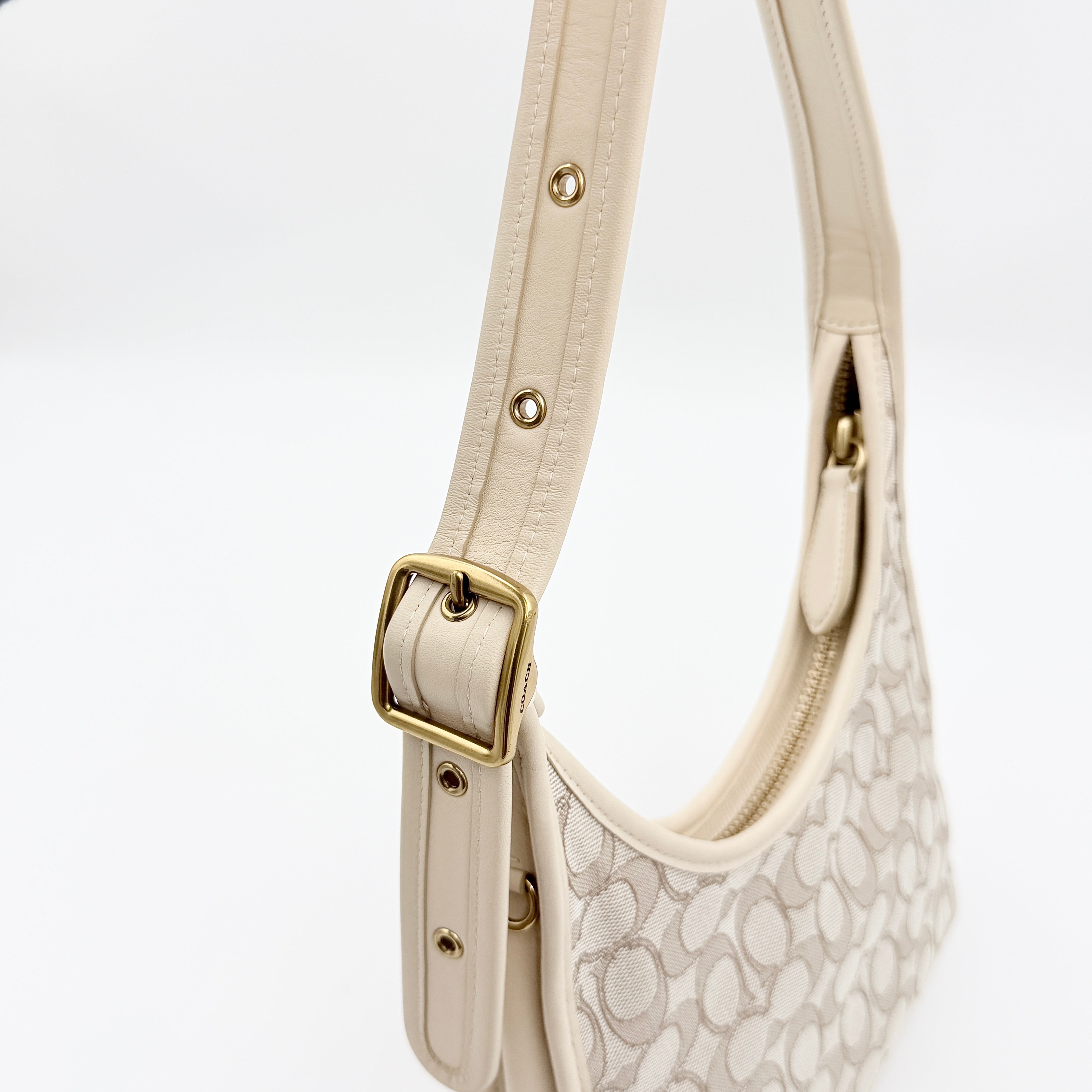 Coach Signature Ergo Shoulder Bag in beige and cream canvas with cream leather trim and brass adjustable buckle, displayed on a white background.