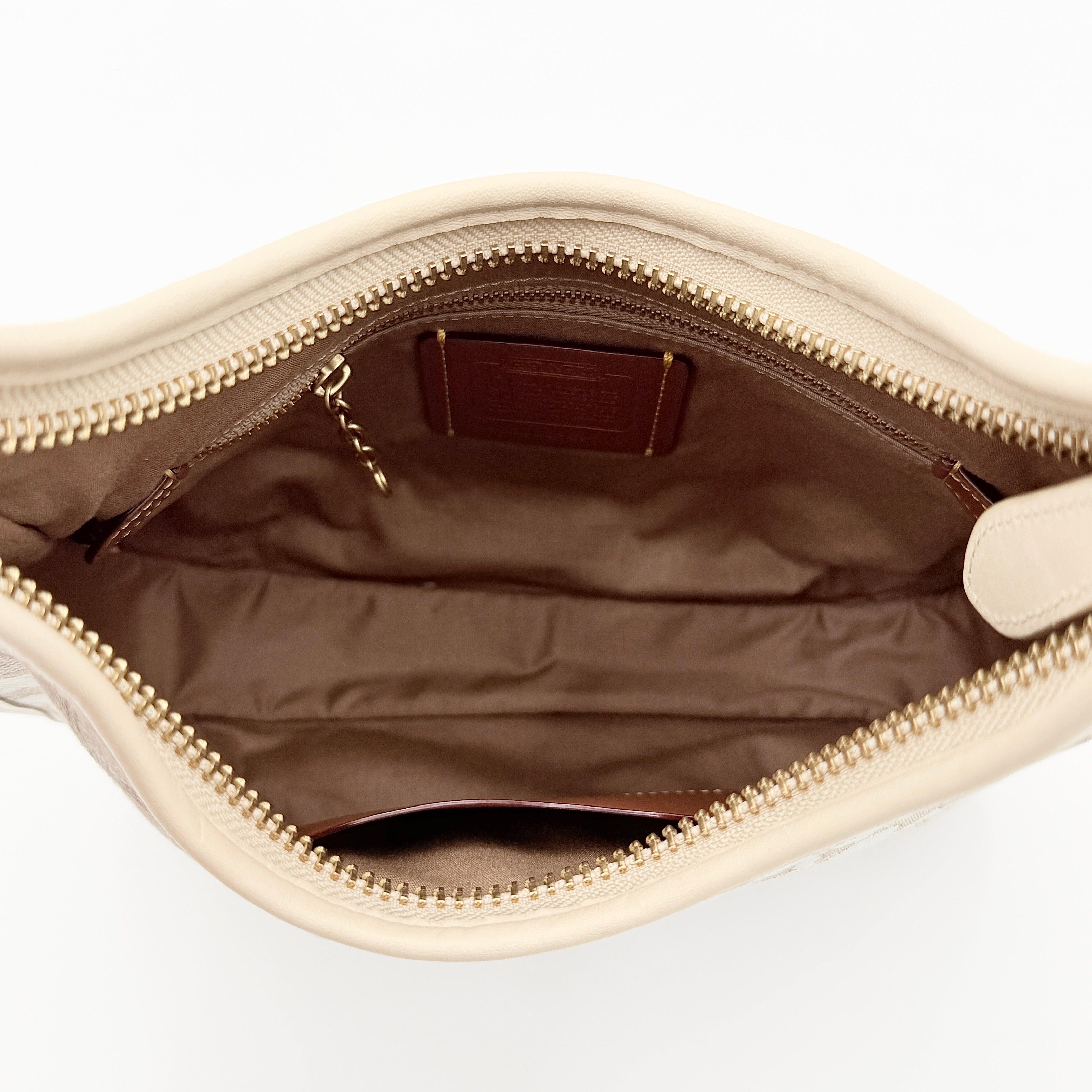 Coach Signature Ergo Shoulder Bag in beige and cream canvas with cream leather trim and brass adjustable buckle, displayed on a white background.