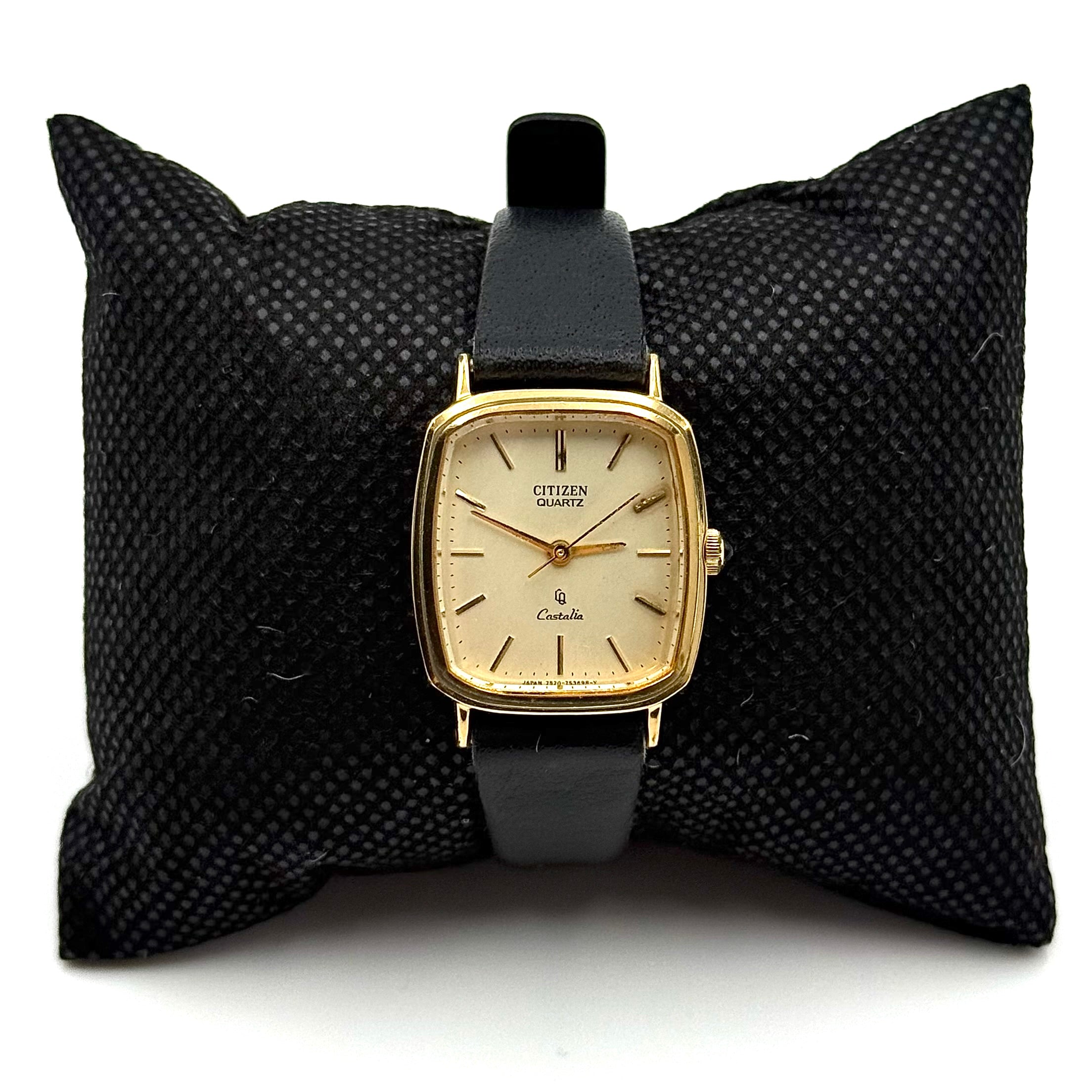 Citizen Castalia gold-tone square quartz watch with a champagne dial and black leather strap displayed on a black cushion.