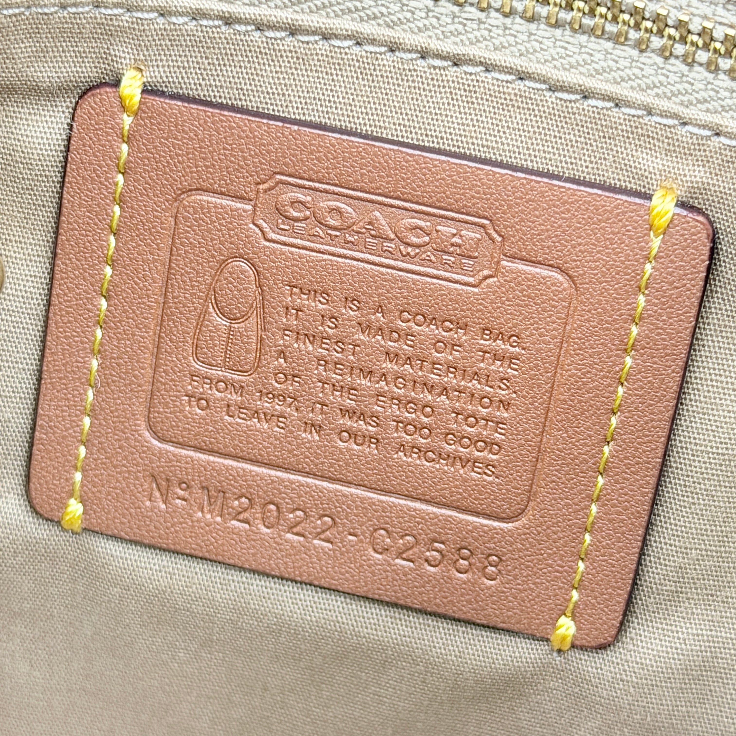 Coach Signature Ergo Shoulder Bag in beige and cream canvas with cream leather trim and brass adjustable buckle, displayed on a white background.