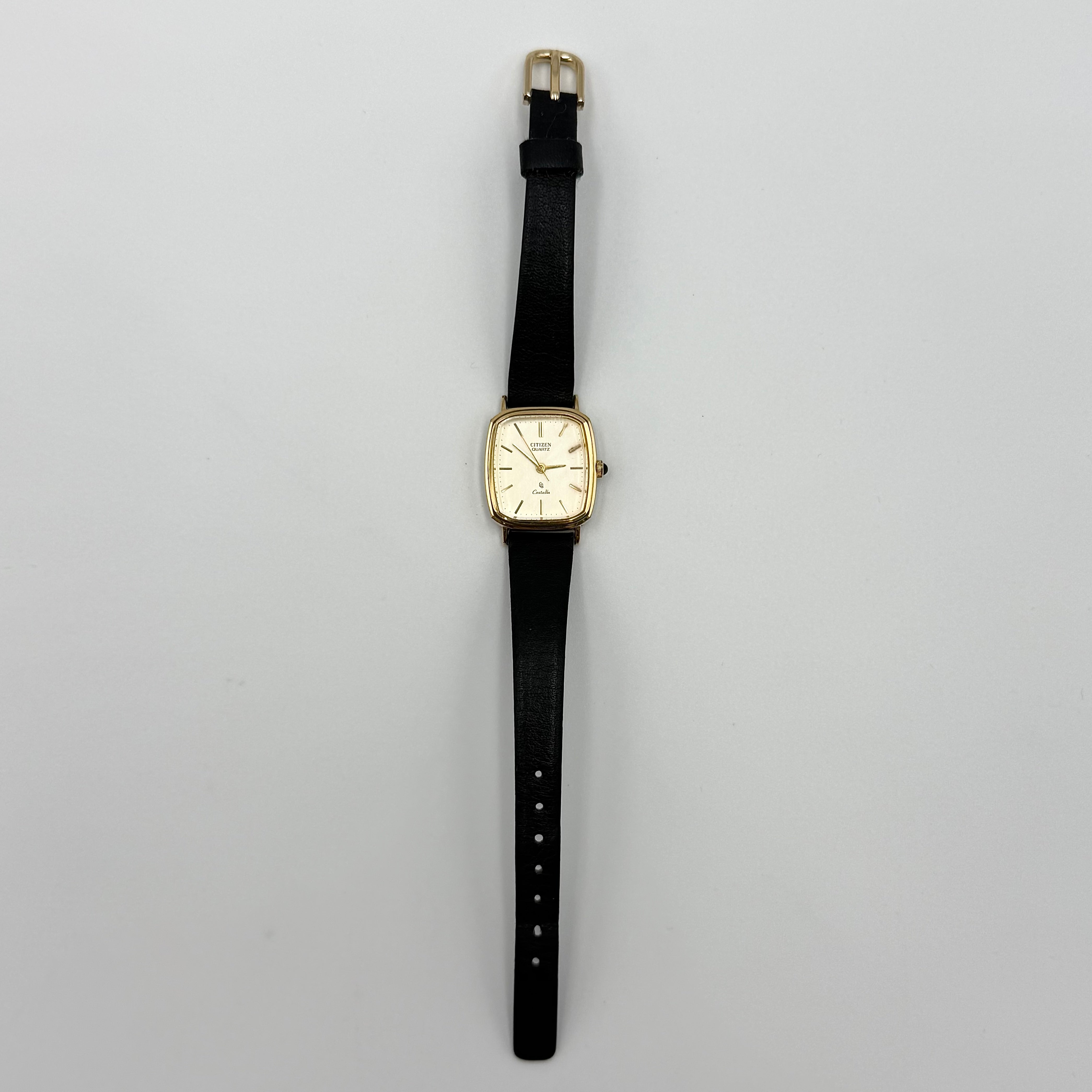 Citizen Castalia gold-tone square quartz watch with a champagne dial and black leather strap displayed on a black cushion.