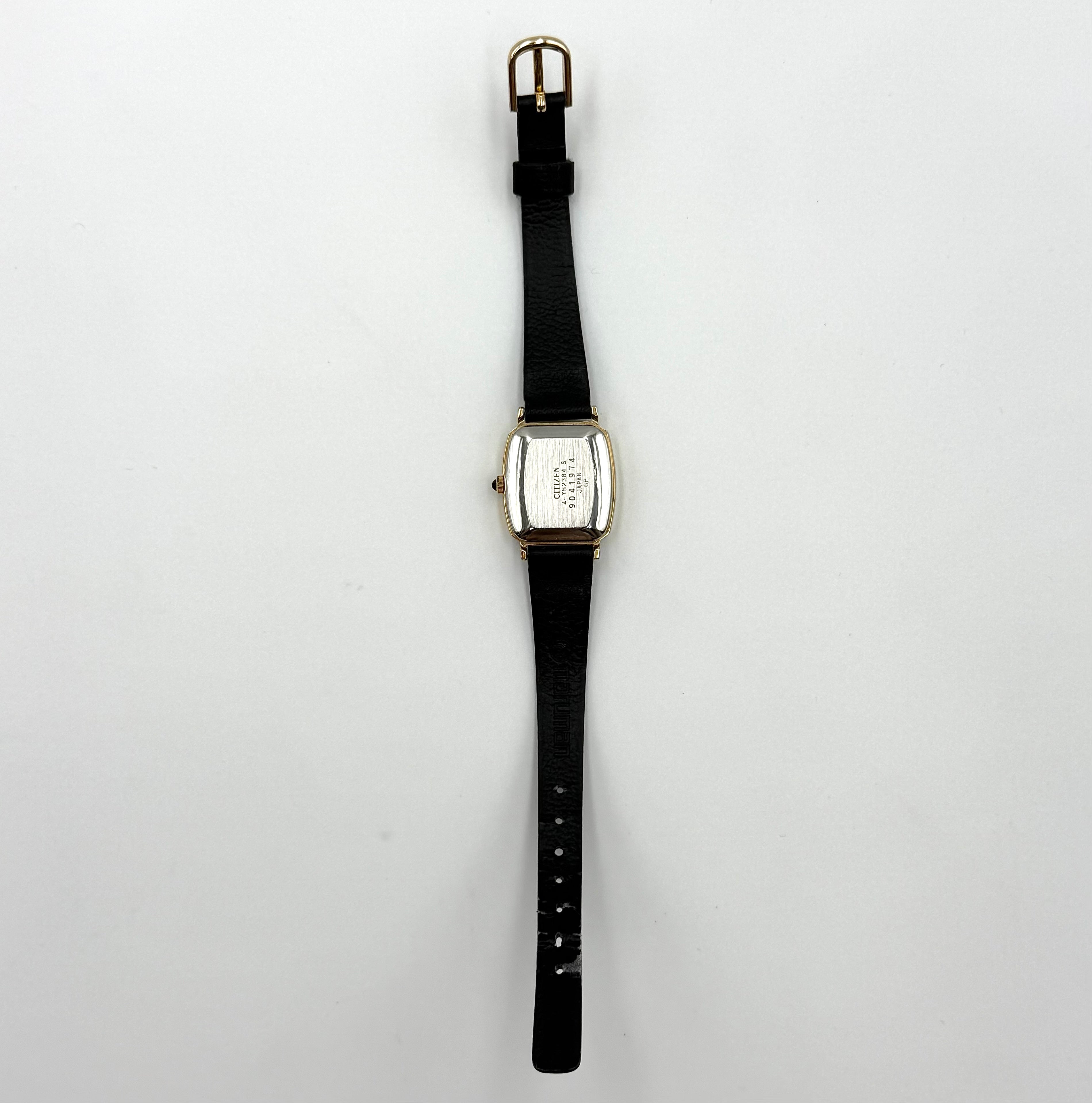 Citizen Castalia gold-tone square quartz watch with a champagne dial and black leather strap displayed on a black cushion.