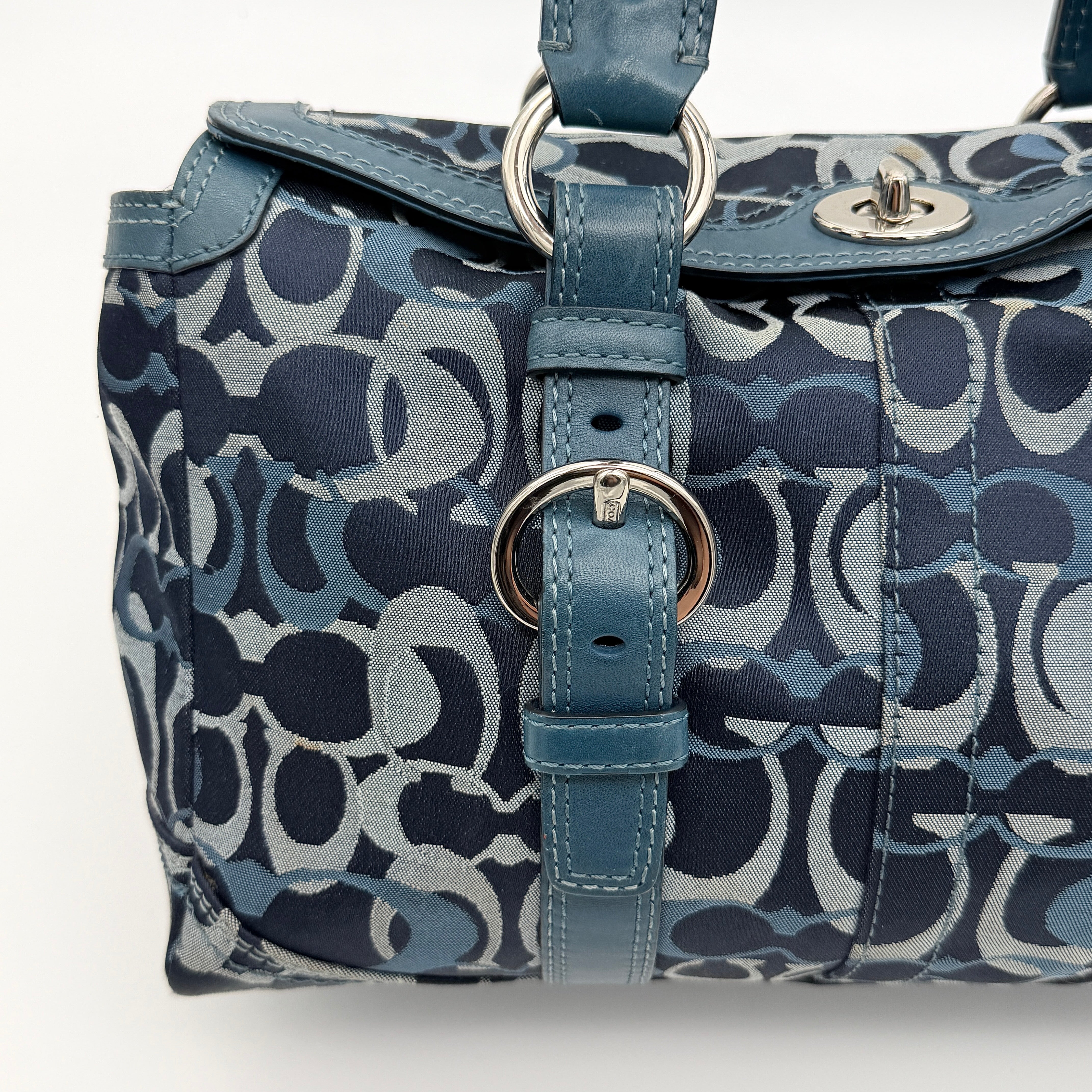 Coach Signature Chelsea Optic Satchel in blue canvas with leather braided handles and silver hardware, displayed on a Coach dust bag.