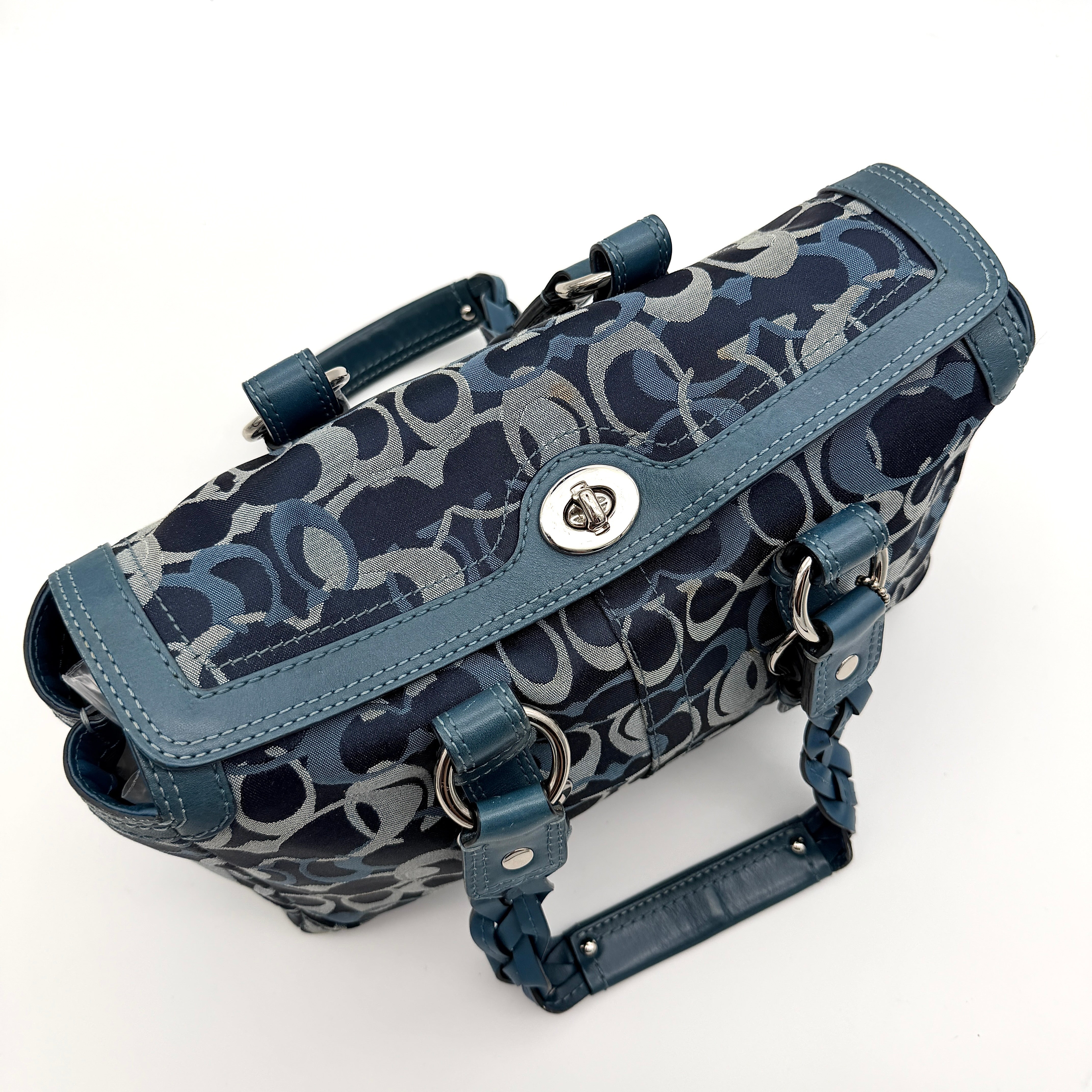 Coach Signature Chelsea Optic Satchel in blue canvas with leather braided handles and silver hardware, displayed on a Coach dust bag.