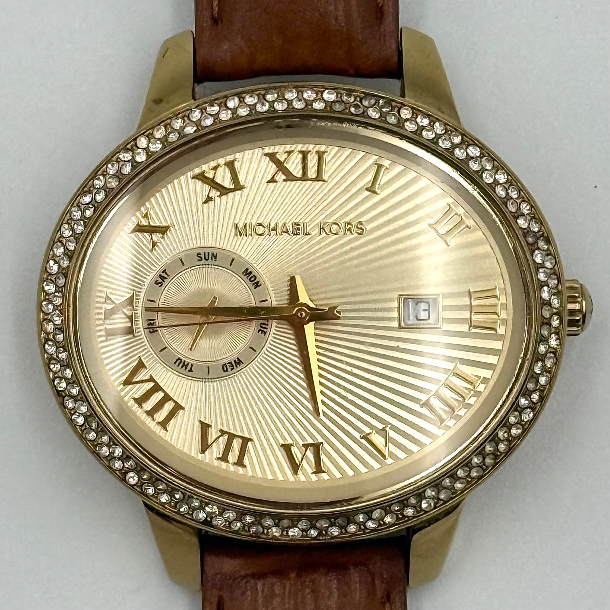 Michael Kors Whitley MK2428 watch with gold dial, crystal bezel and brown leather strap on black cushion