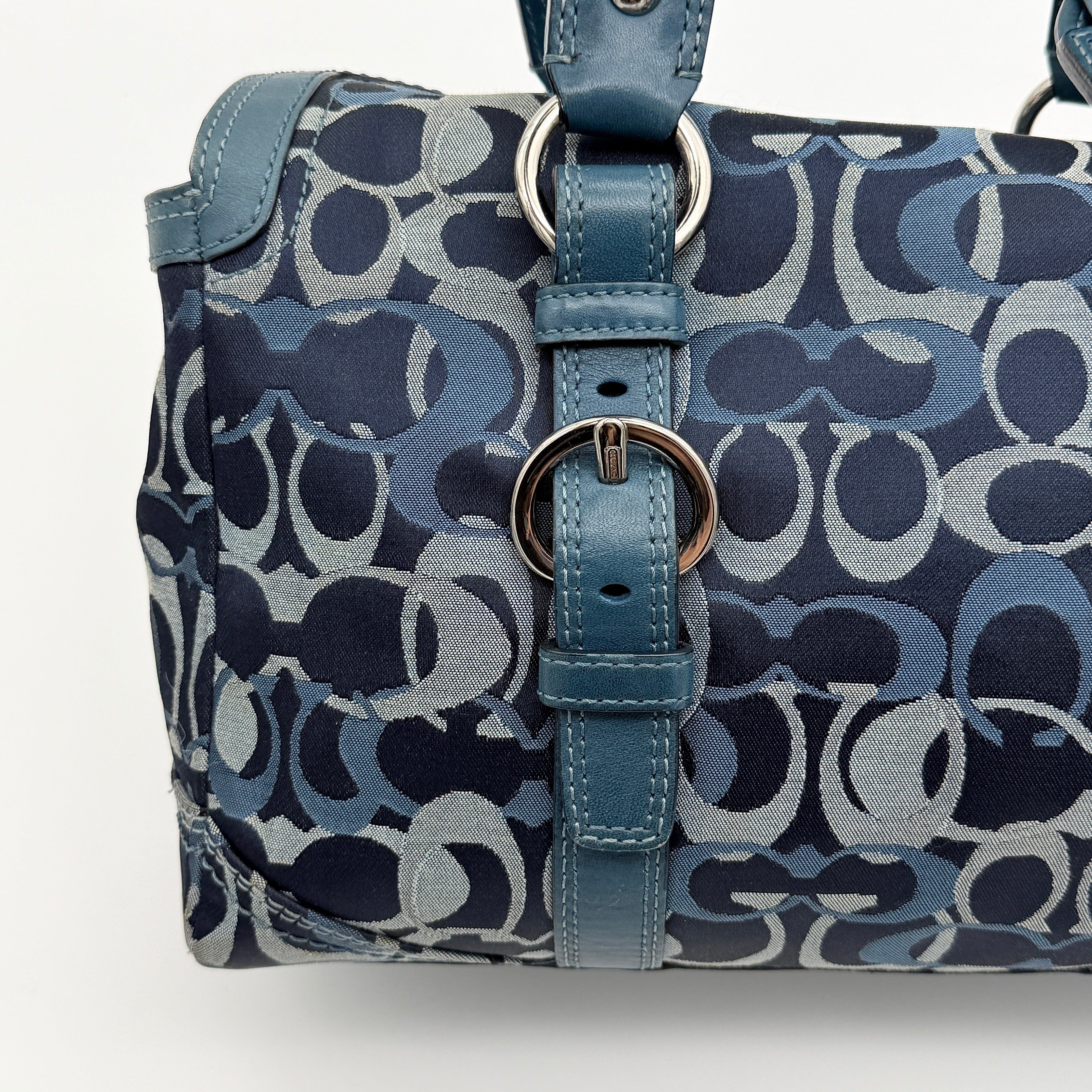 Coach Signature Chelsea Optic Satchel in blue canvas with leather braided handles and silver hardware, displayed on a Coach dust bag.