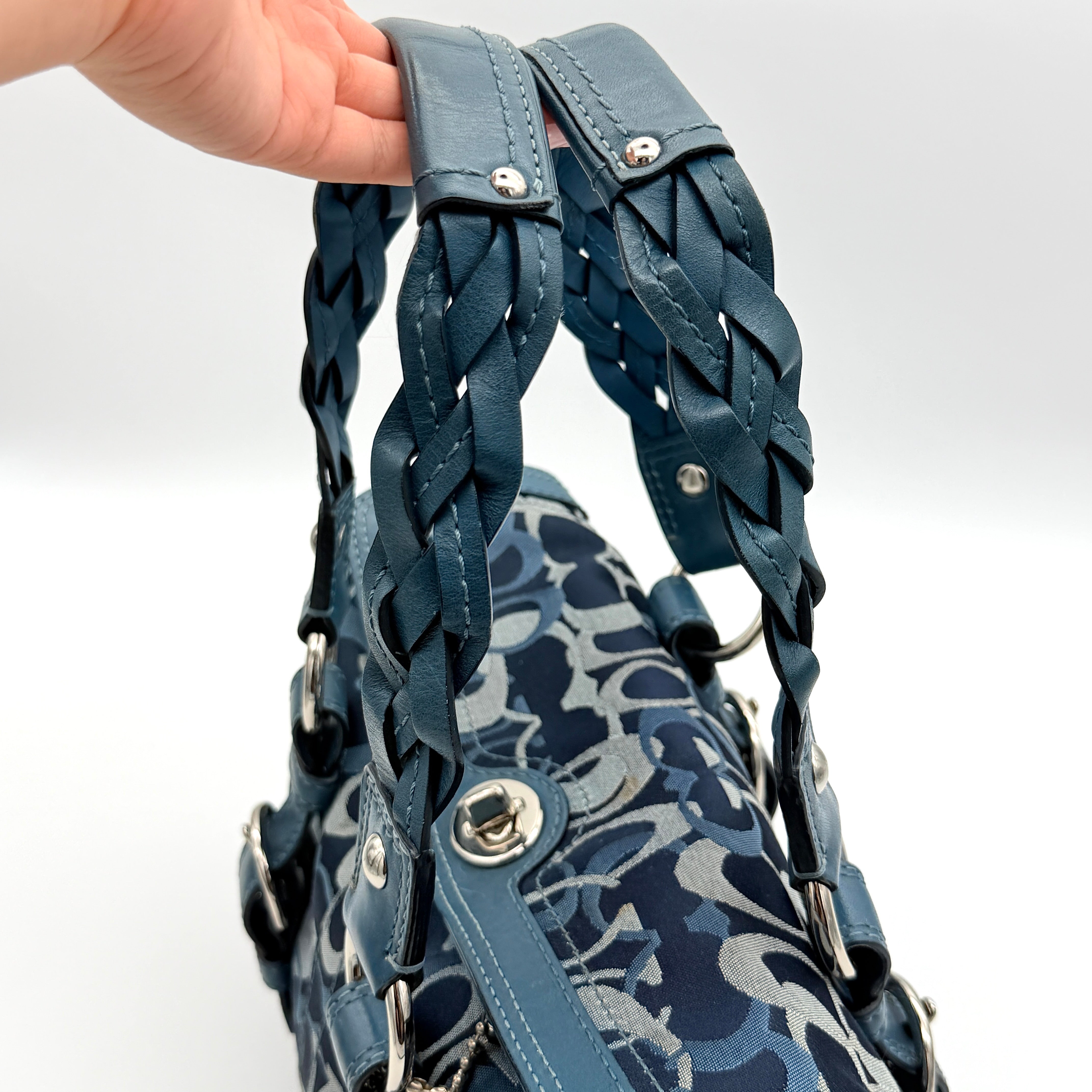 Coach Signature Chelsea Optic Satchel in blue canvas with leather braided handles and silver hardware, displayed on a Coach dust bag.